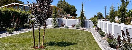 A lush green yard with a white fence and trees.