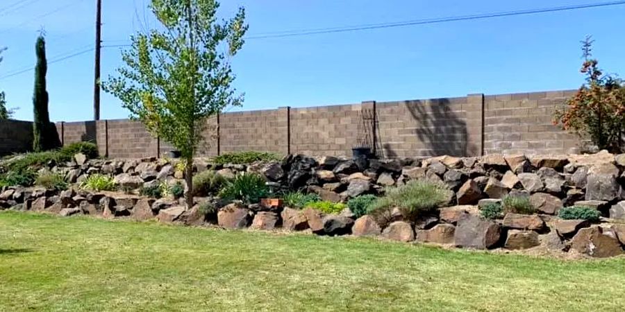 A large rock wall surrounds a lush green lawn in a backyard.