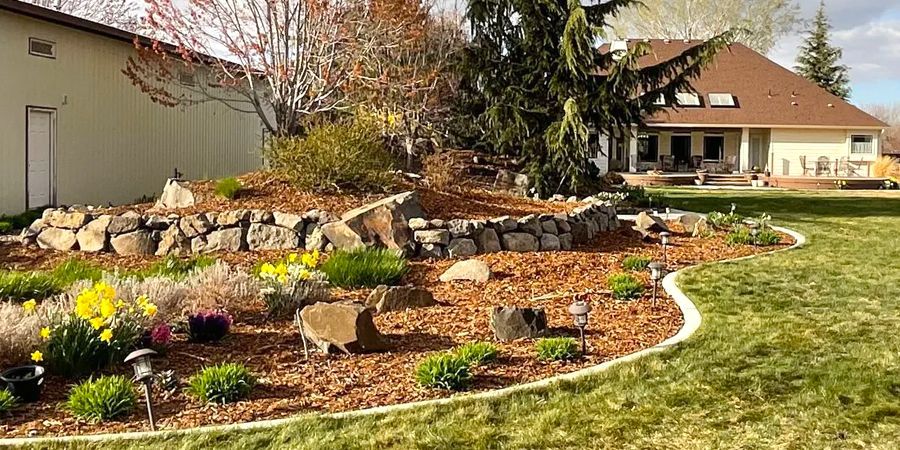 A house with a large lawn and a rock garden in front of it.