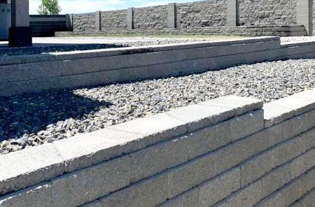 A brick wall with gravel in the background and a fence in the background.