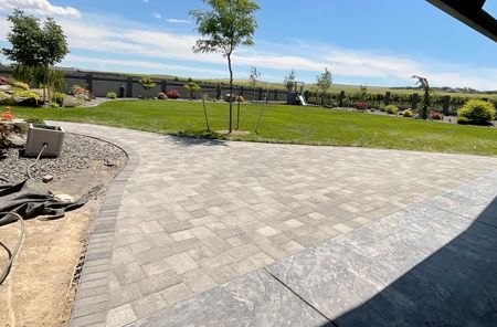 A brick driveway leading to a lush green field.
