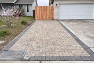 A brick driveway leading to a house with a wooden fence.
