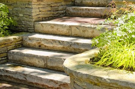 A set of stone stairs leading up to a stone wall surrounded by plants.