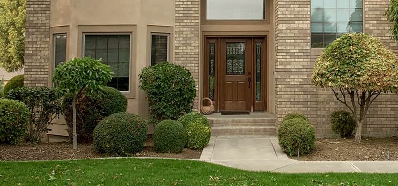 The front of a brick house with a wooden door and a lush green lawn.