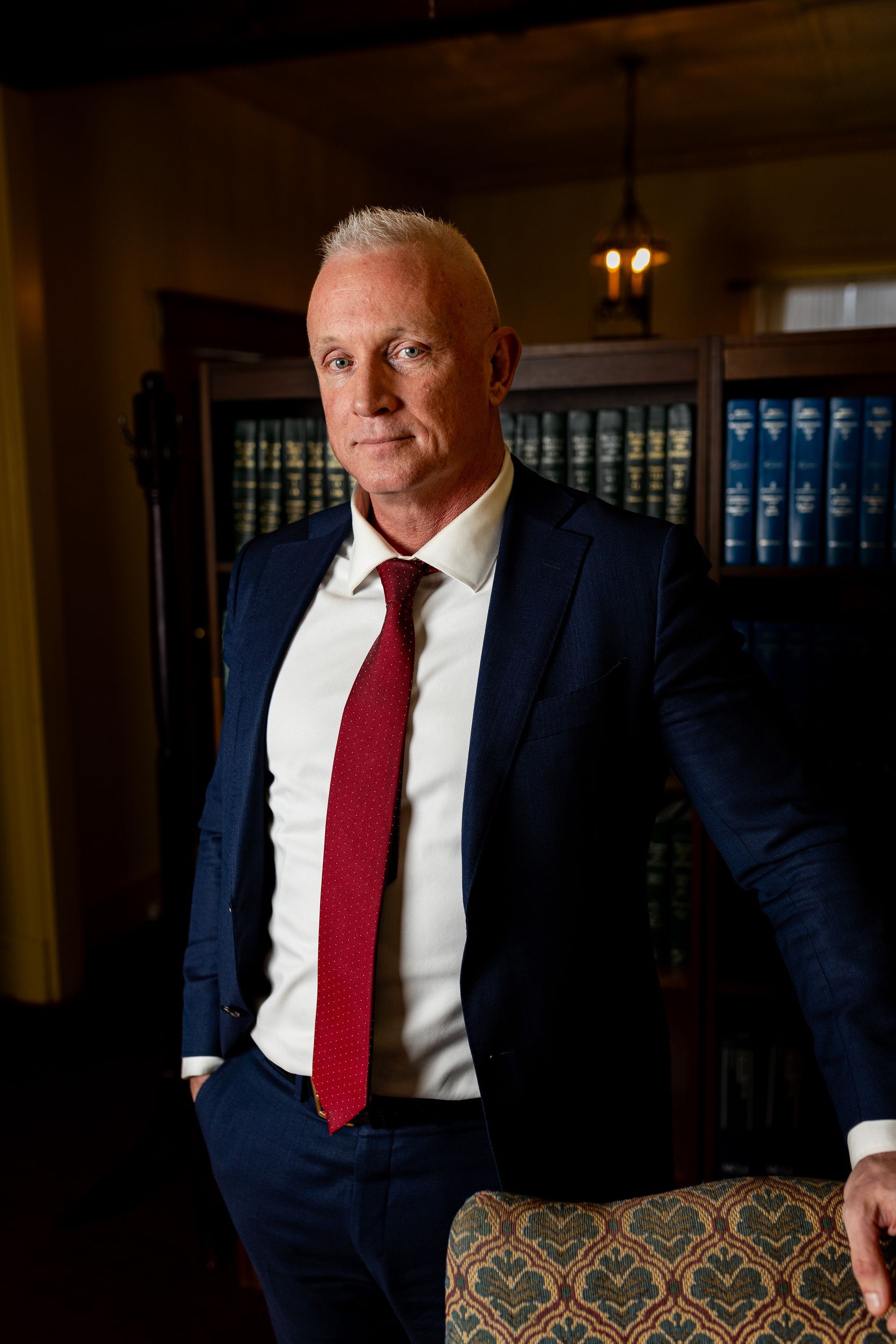 Photography MA -A man in a suit and tie is standing in front of a bookshelf.