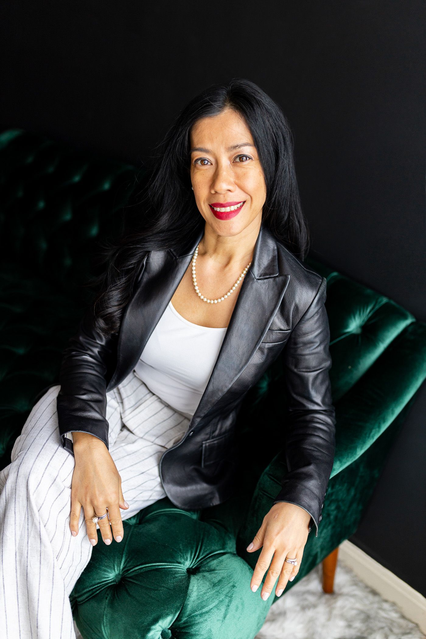 Photography MA -A woman in a black jacket and white dress is sitting in a green chair.