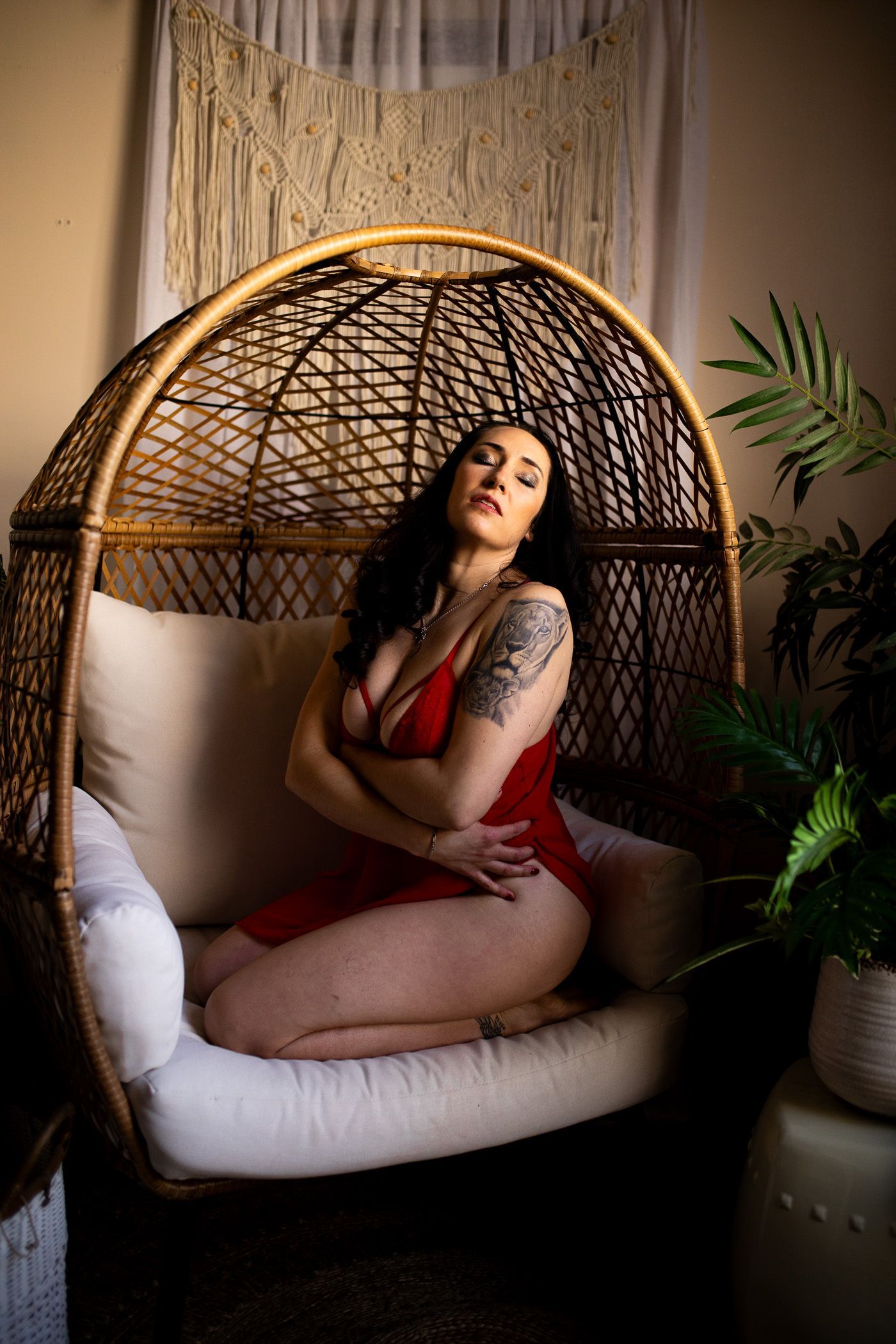 Boudoir moody image of a woman in red teddy kneeling in an egg chair