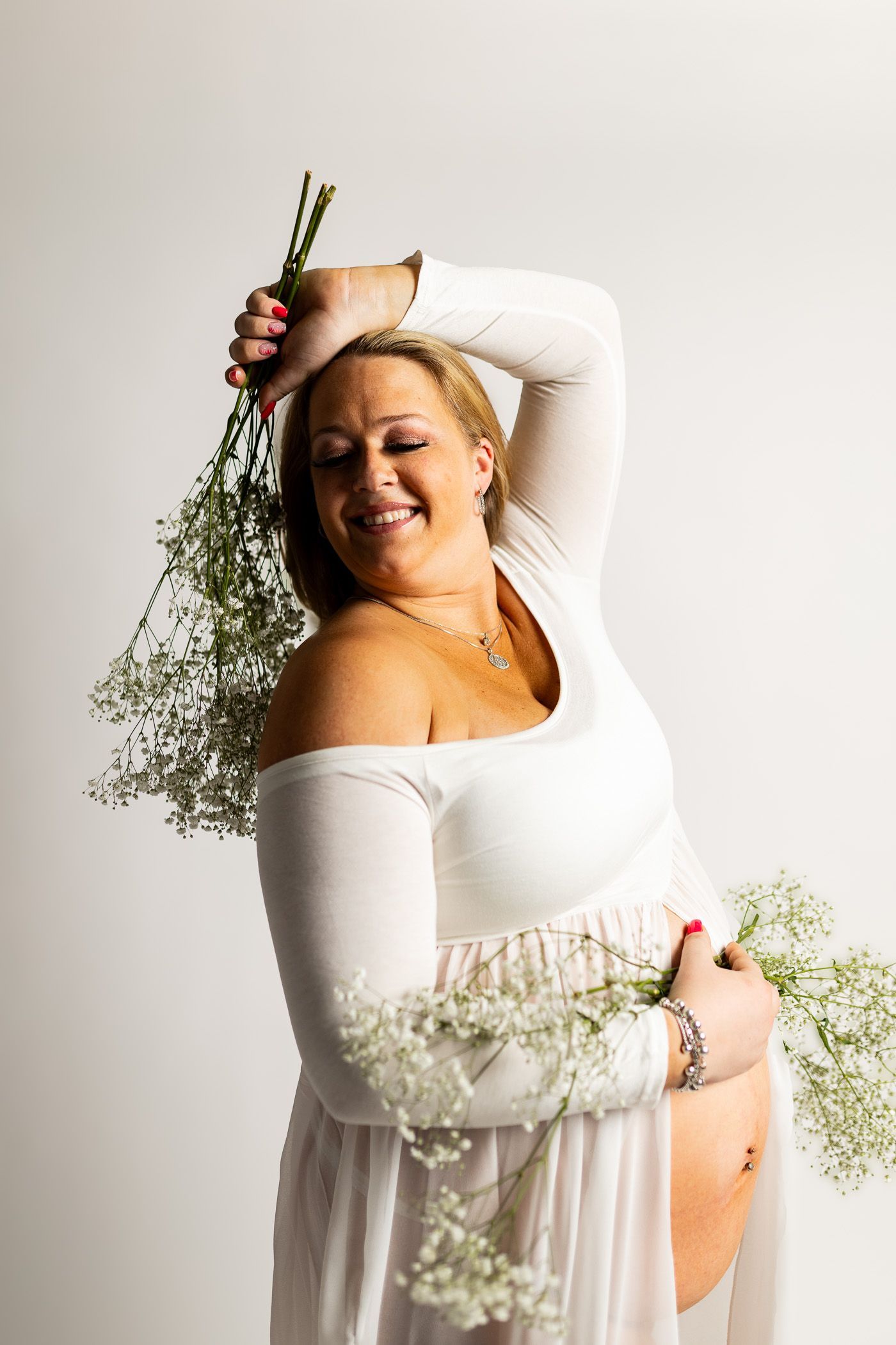 A pregnant woman in a white dress is posing with baby's breath flowers