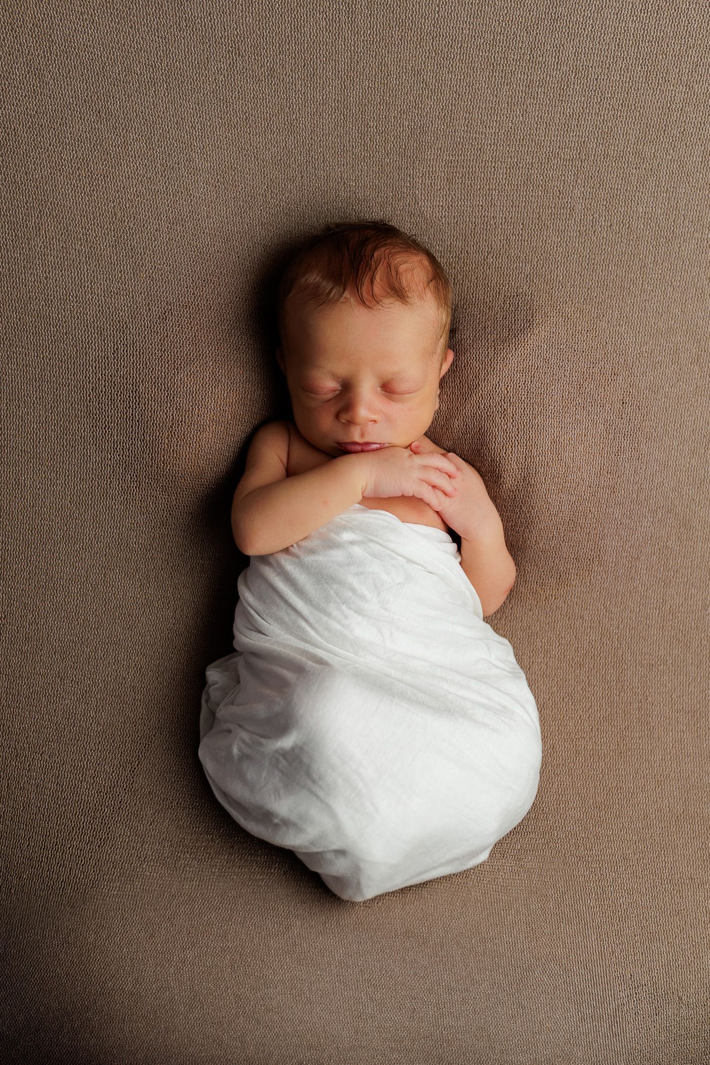 A newborn baby is wrapped in a white blanket on a tan blanket - Minimalistic newborn setup