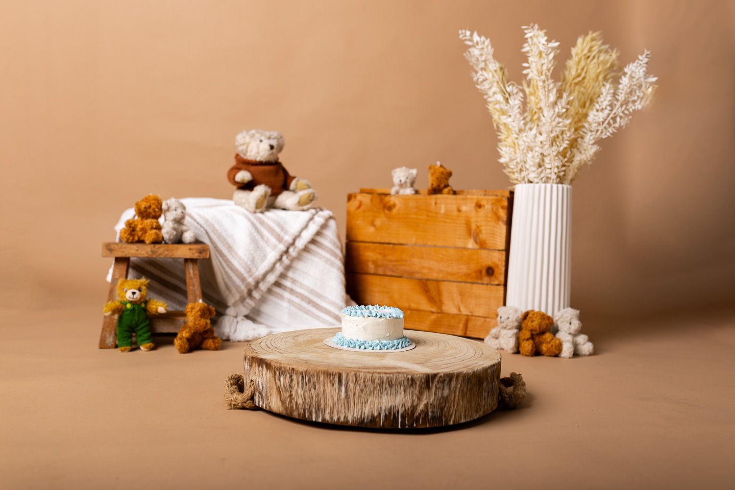 A cake on a wooden stump surrounded by teddy bears and flowers.