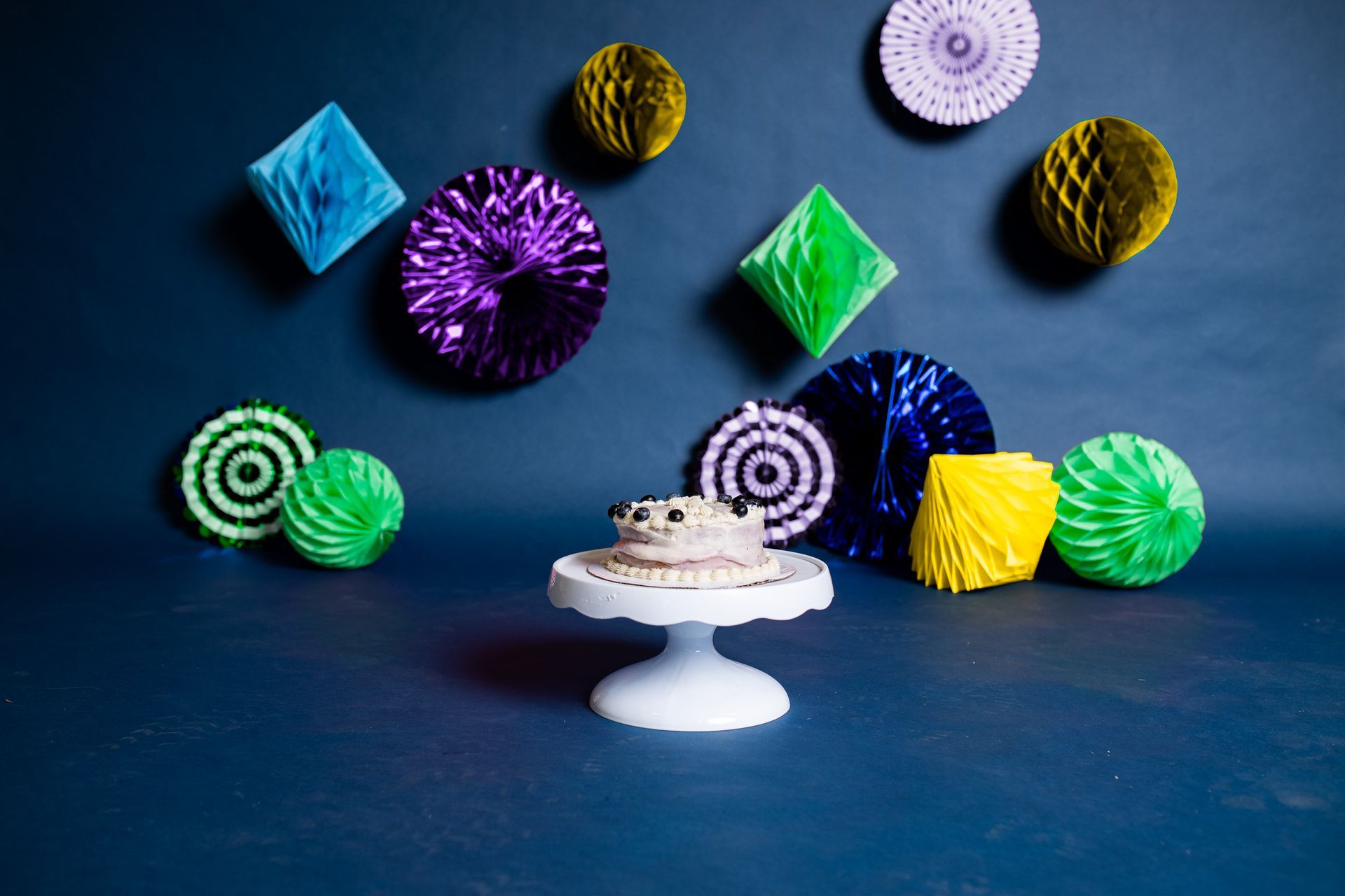 There is a cake on a cake stand in front of a wall with decorations.