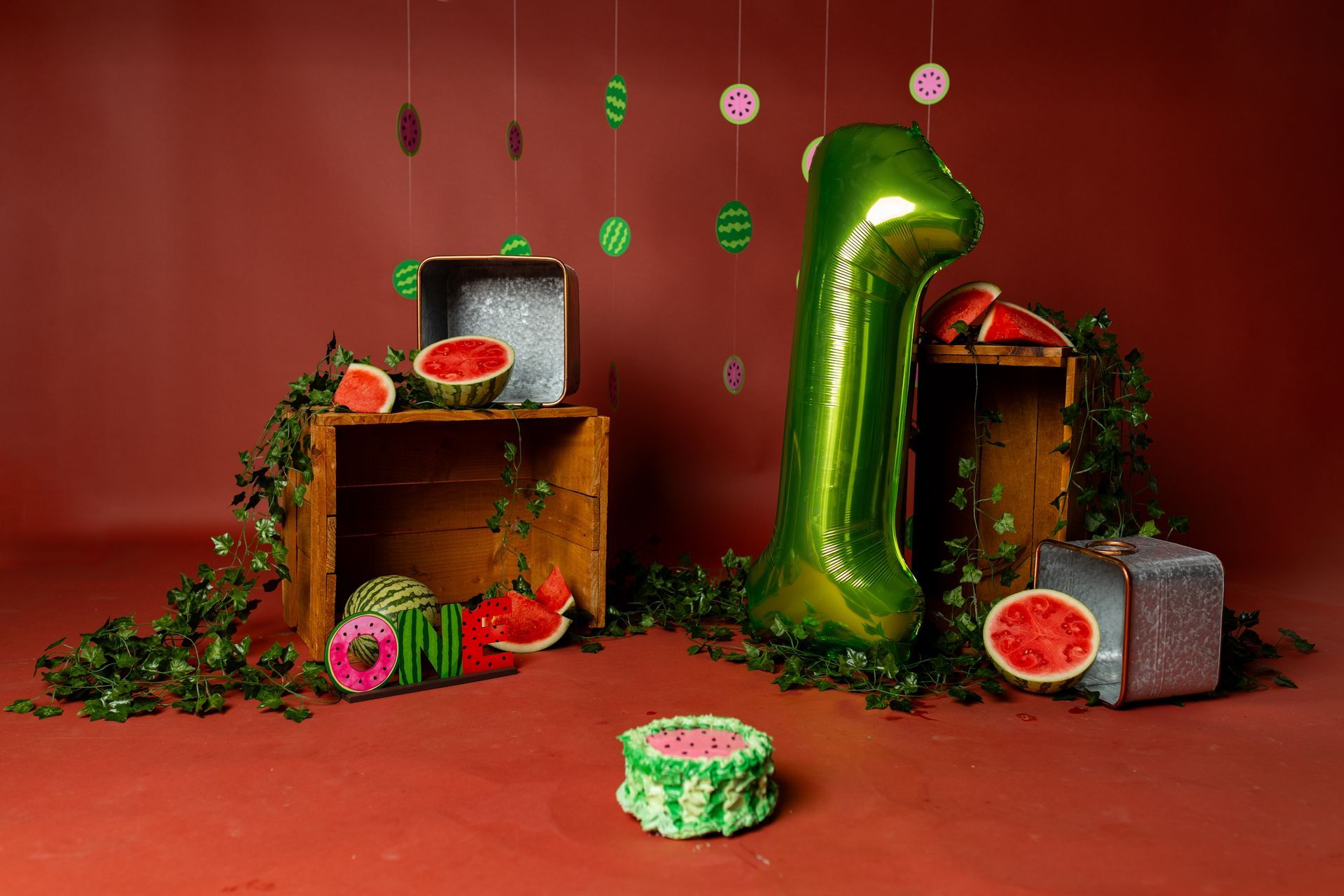 A green number one balloon is surrounded by watermelons and a cake.