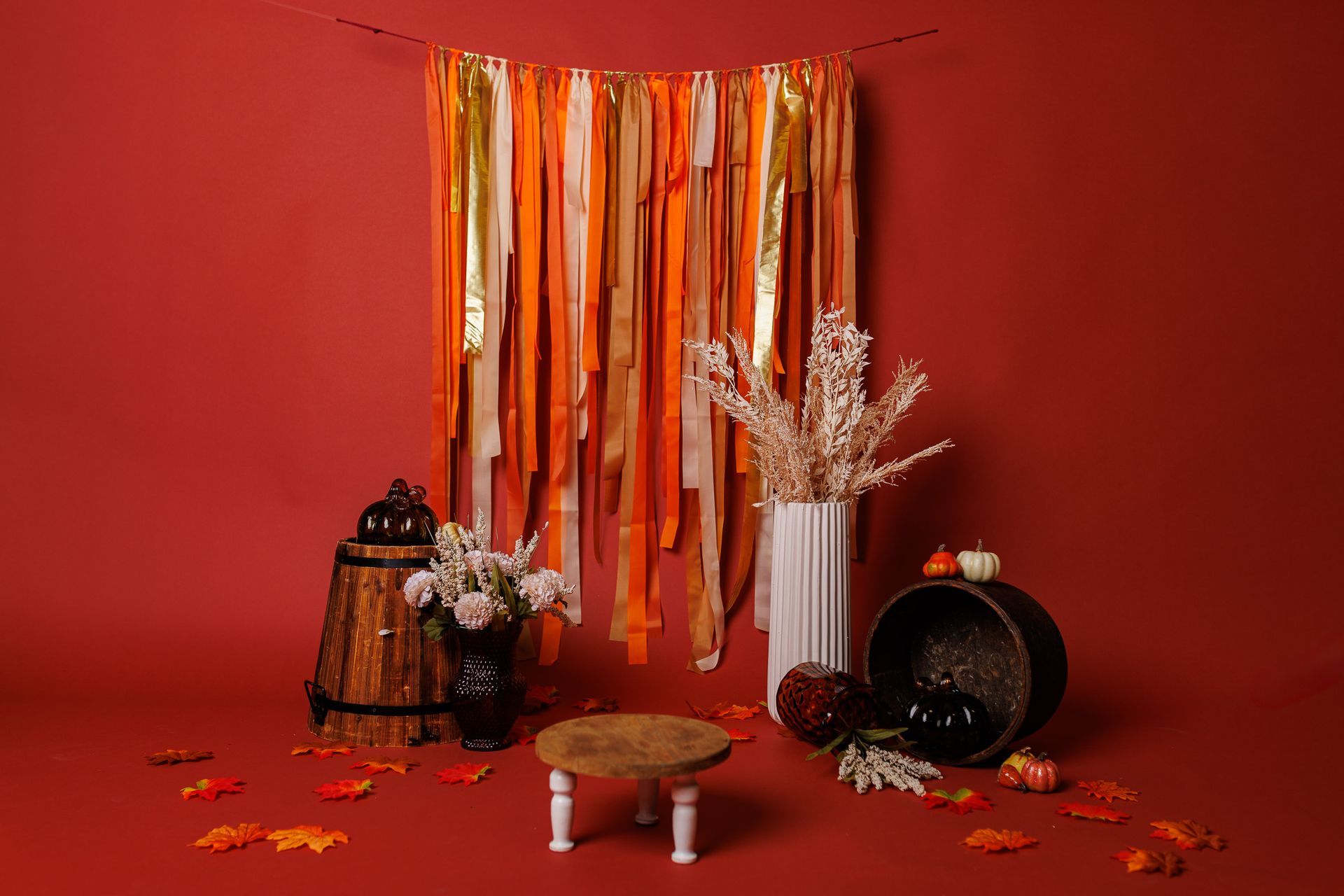 A room with a red wall , a table , a vase of flowers , pumpkins and leaves.