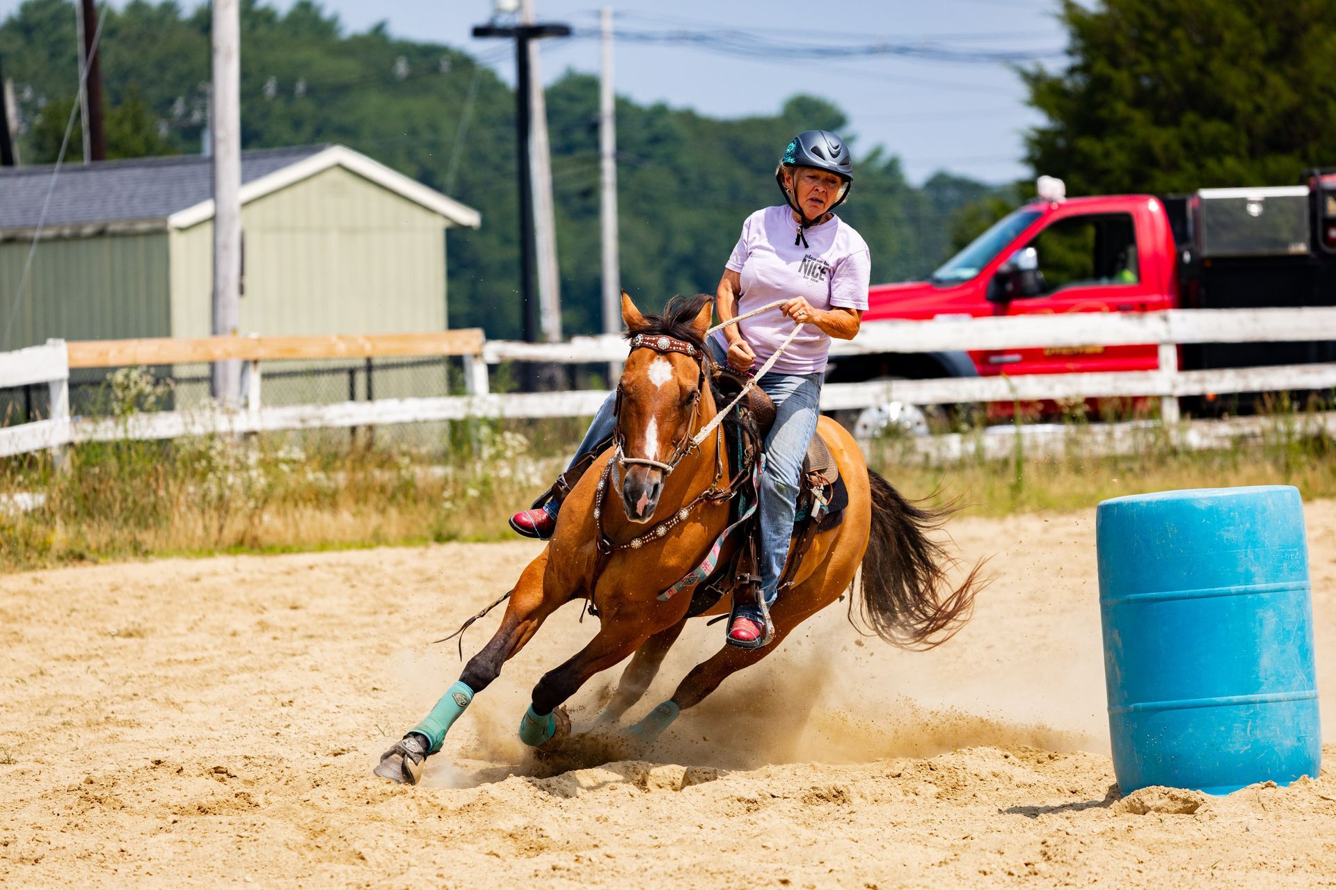 A woman is riding a brown horse around a blue barrel.
