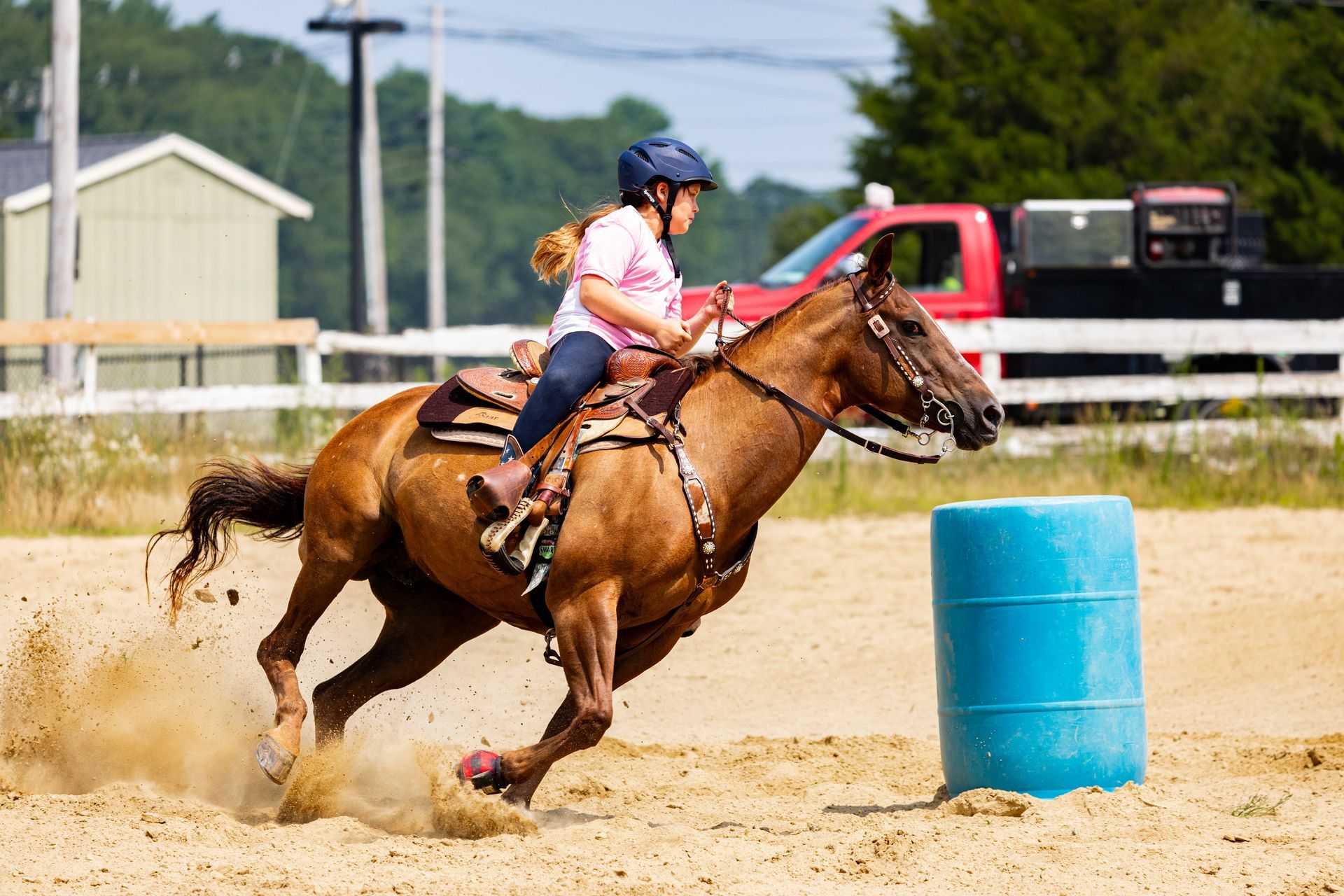 A person is riding a horse around a blue barrel.