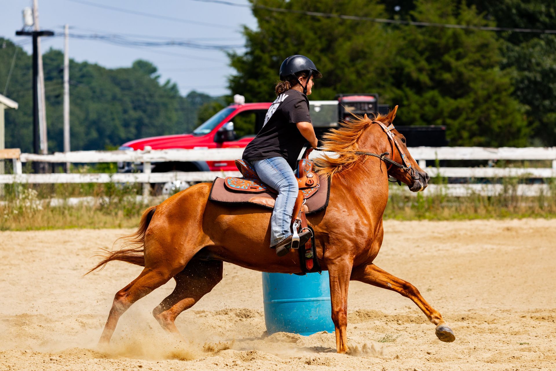 A man is riding a horse around a blue barrel.
