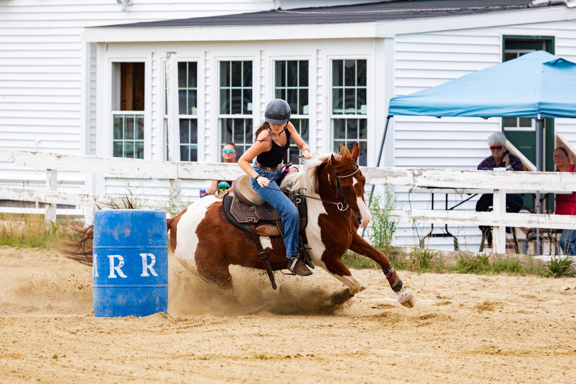 A woman is riding a brown and white horse around a blue barrel.