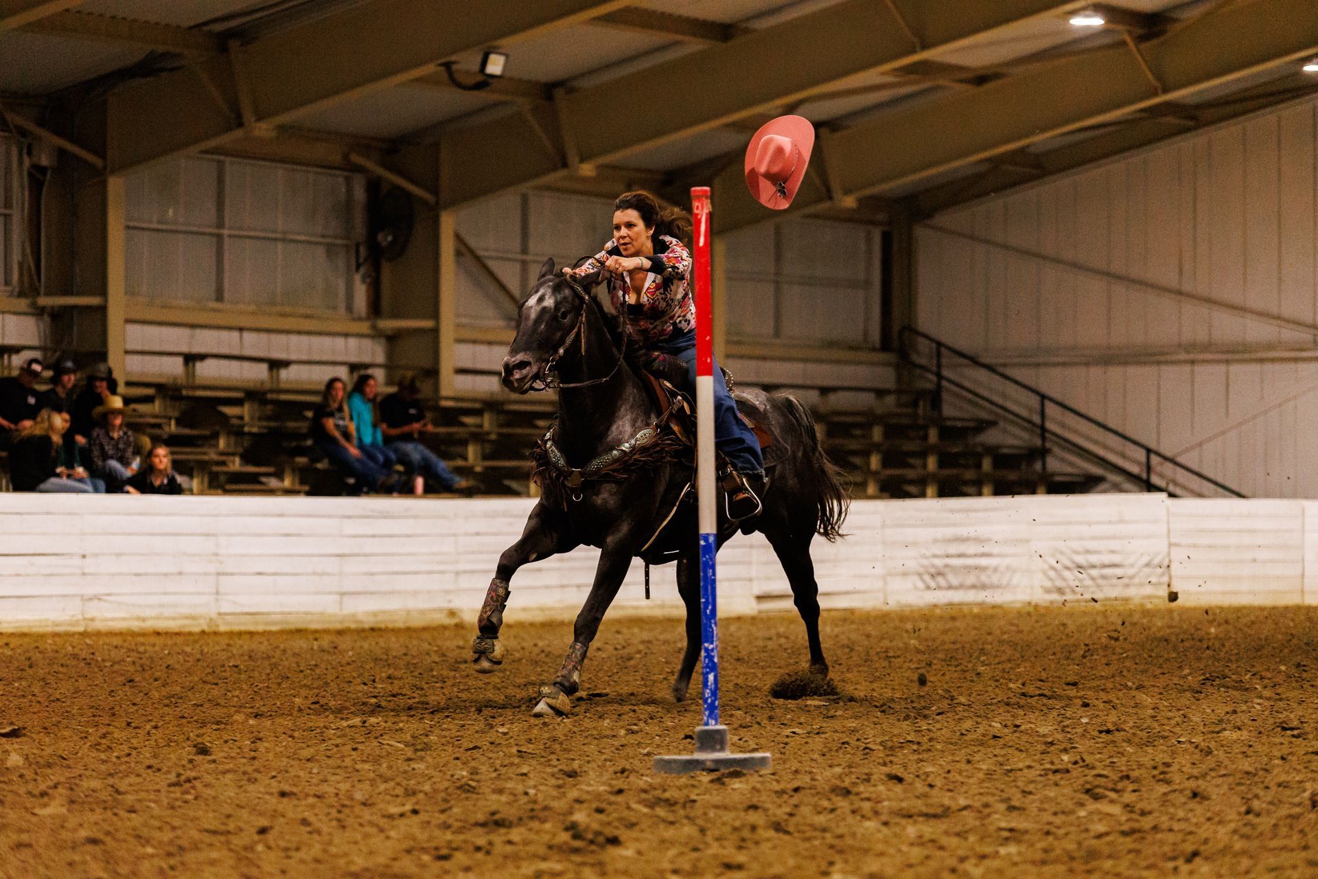 A woman is riding a horse through a pole in a rodeo arena.