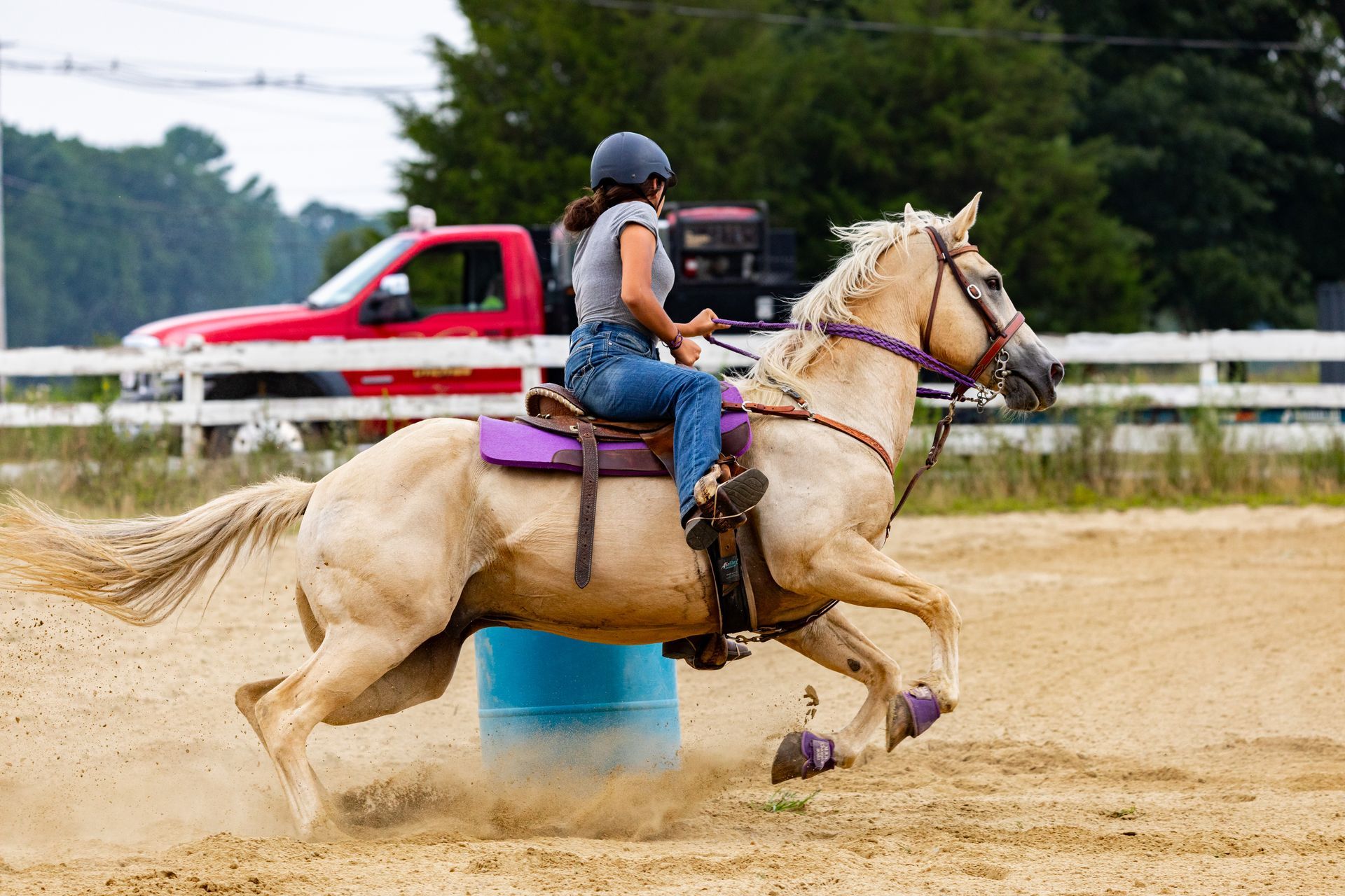 A woman is riding a horse around a barrel in a dirt field.