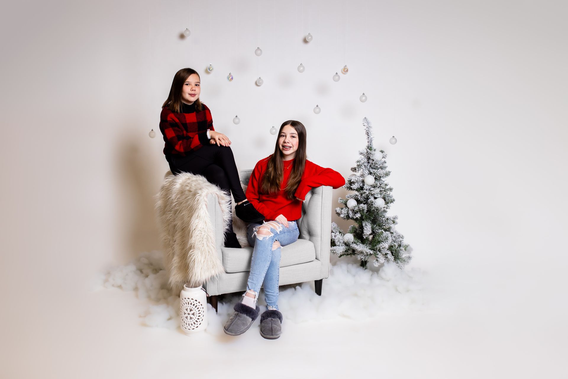 Two girls are sitting on a couch in front of a christmas tree.