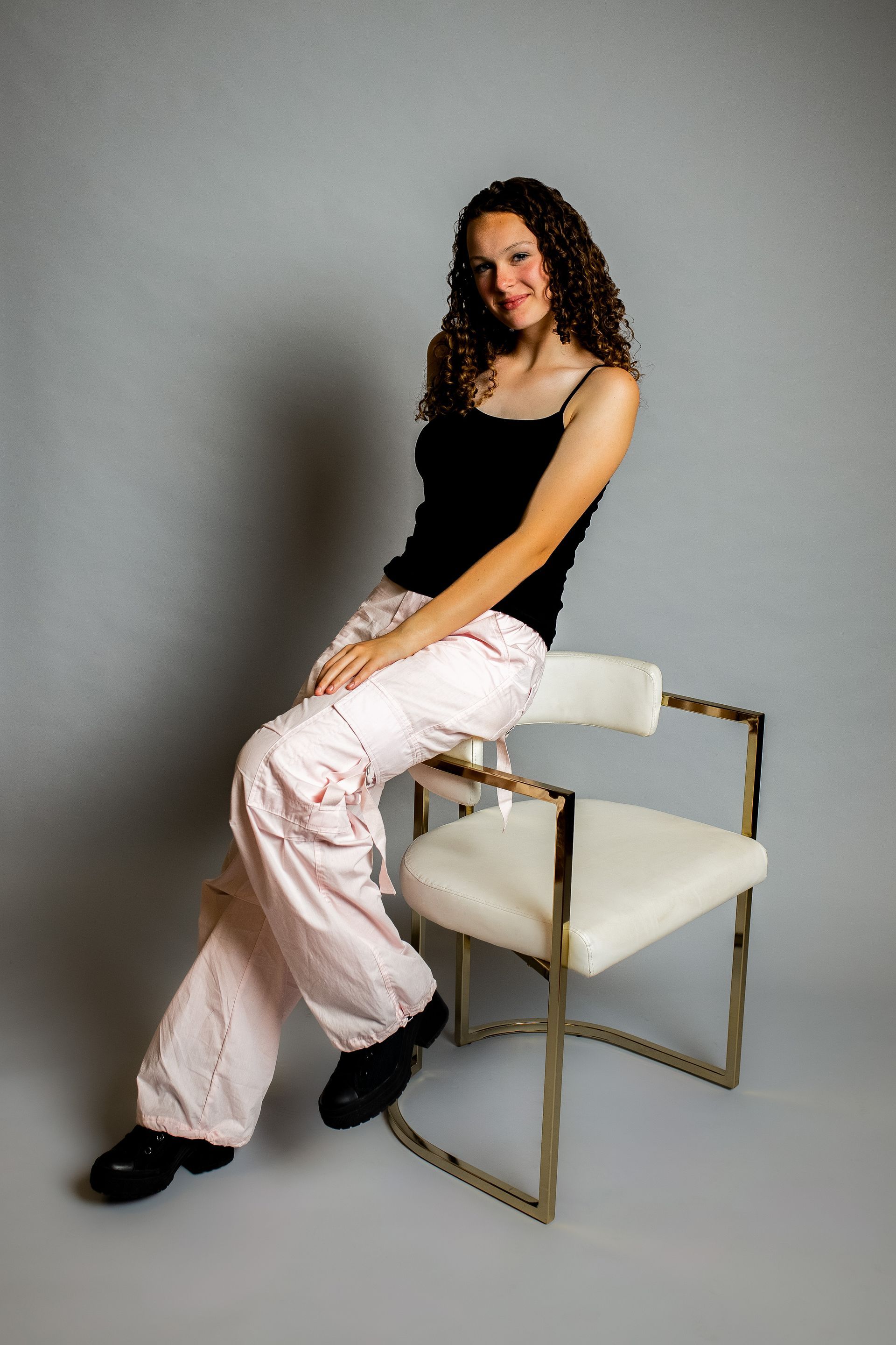 Business portrait - girl in black top and white cargo pants leaning on chair