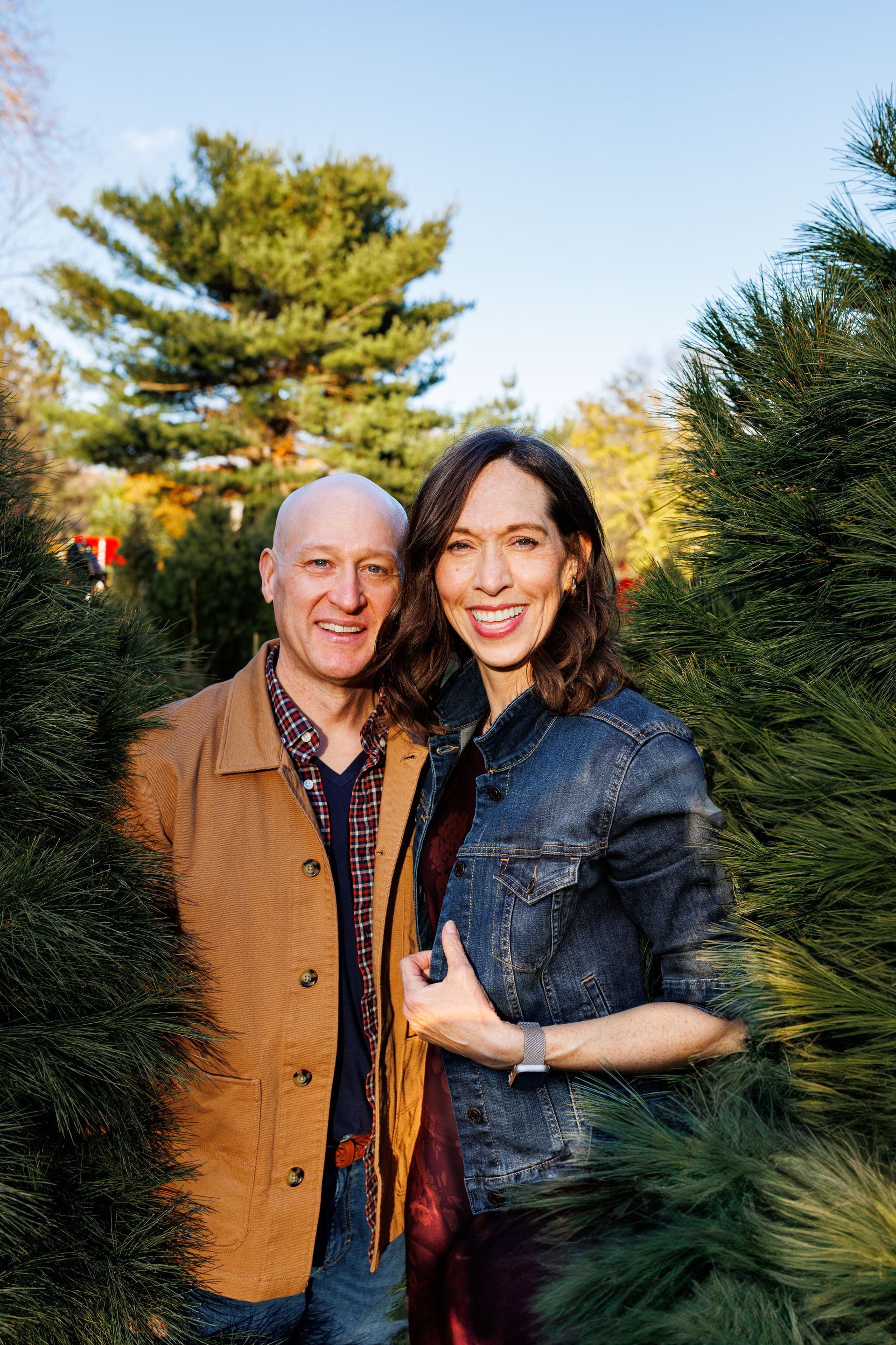 A man and a woman are standing next to each other in a christmas tree farm.
