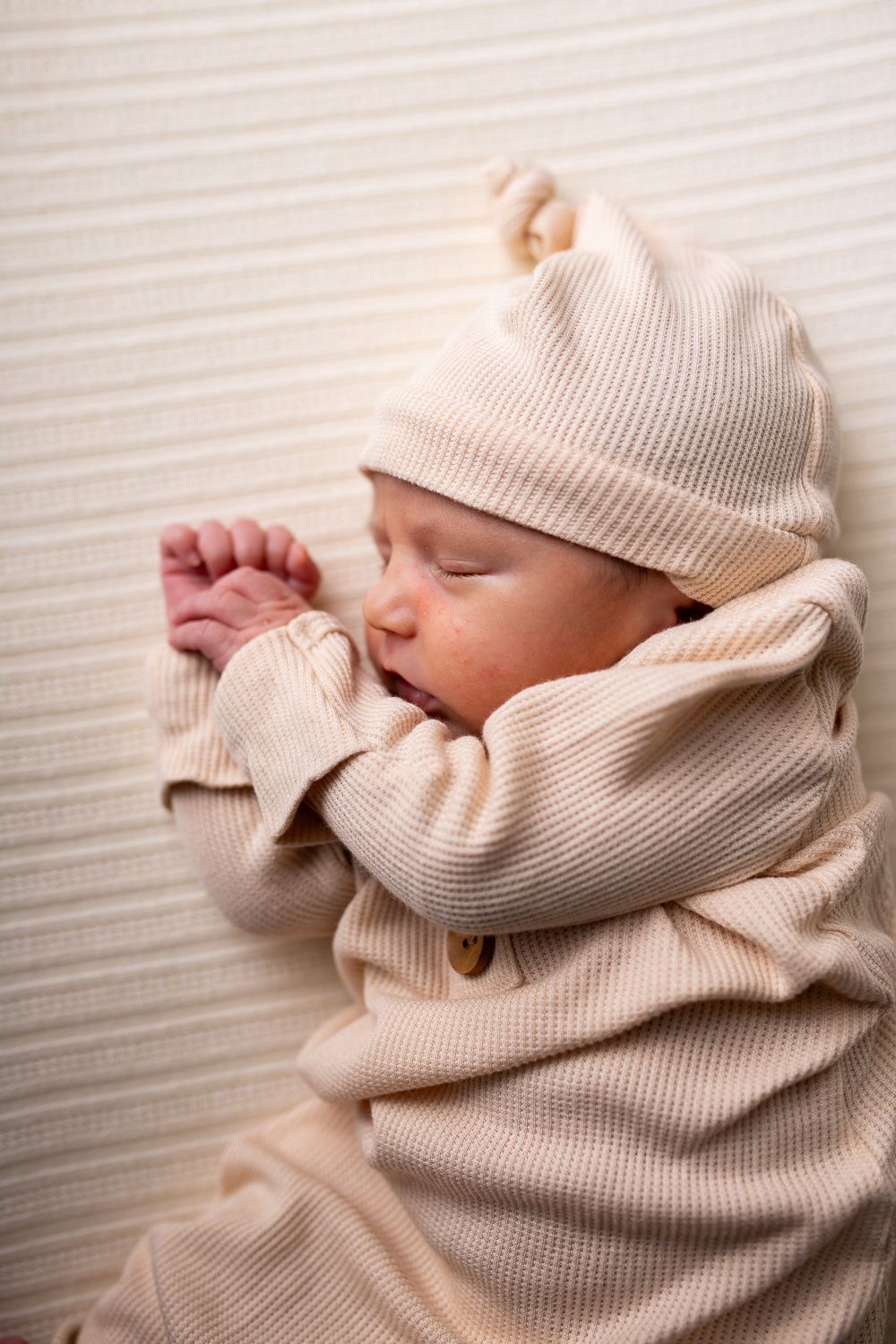 A newborn baby wrapped in a white blanket is sleeping on a red background.