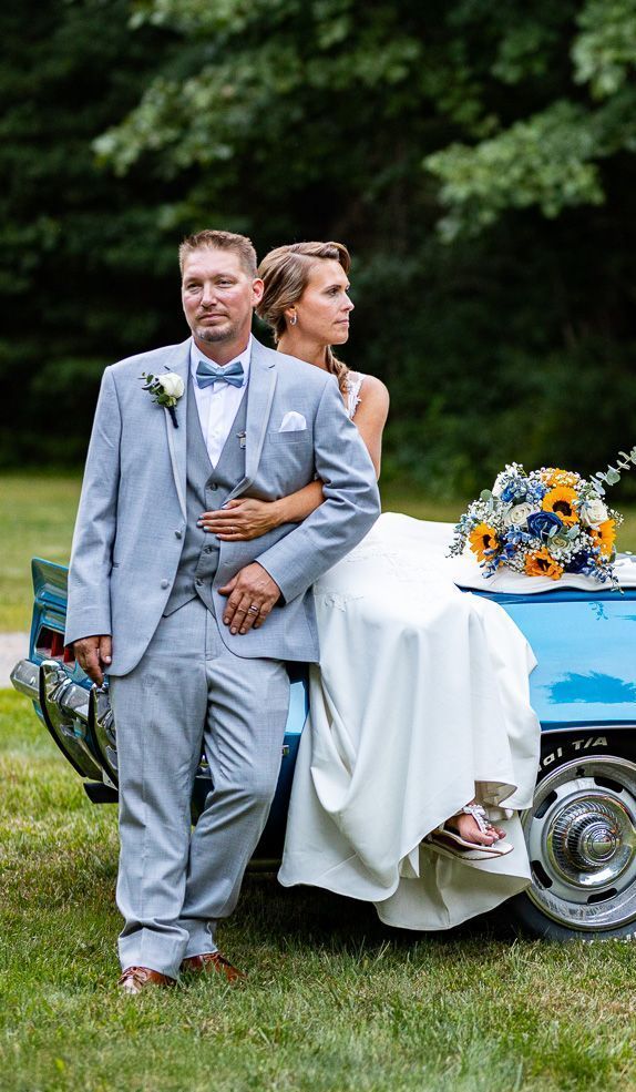 A bride and groom are posing for a picture next to a blue car.