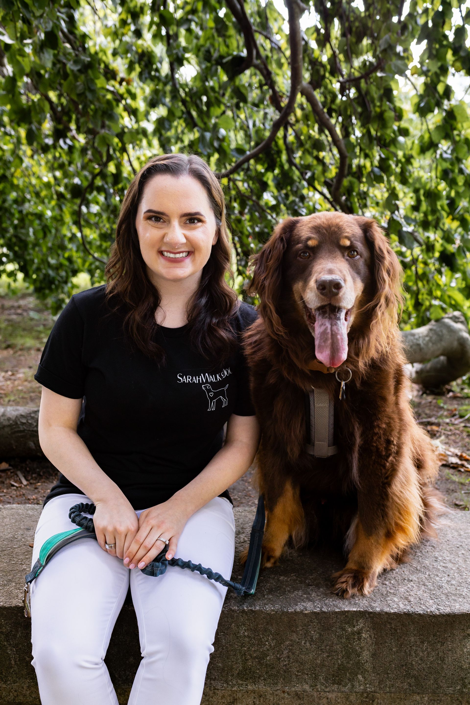 A woman is sitting next to a brown dog on a bench.
