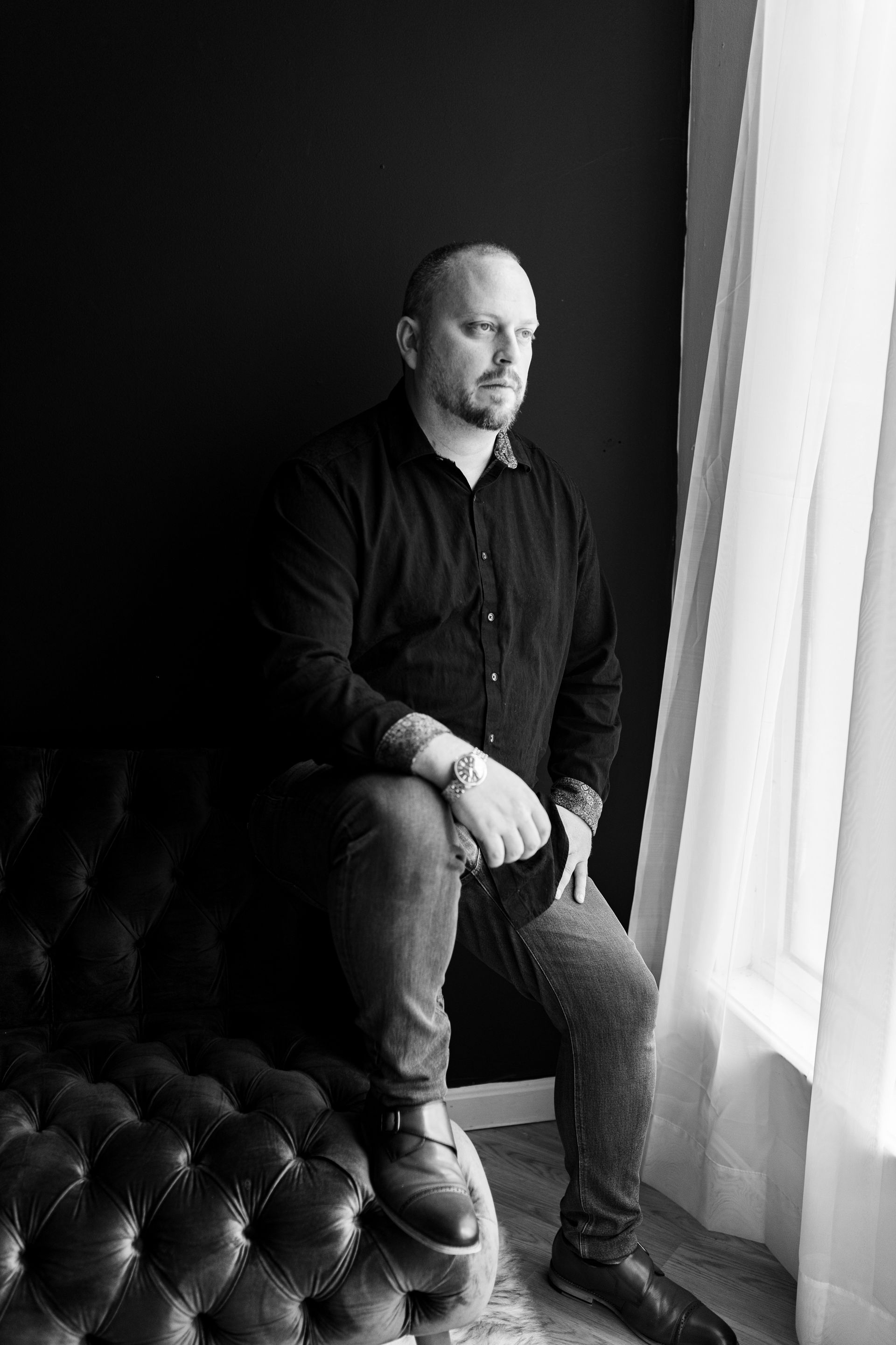 A man is sitting on a couch in front of a window.