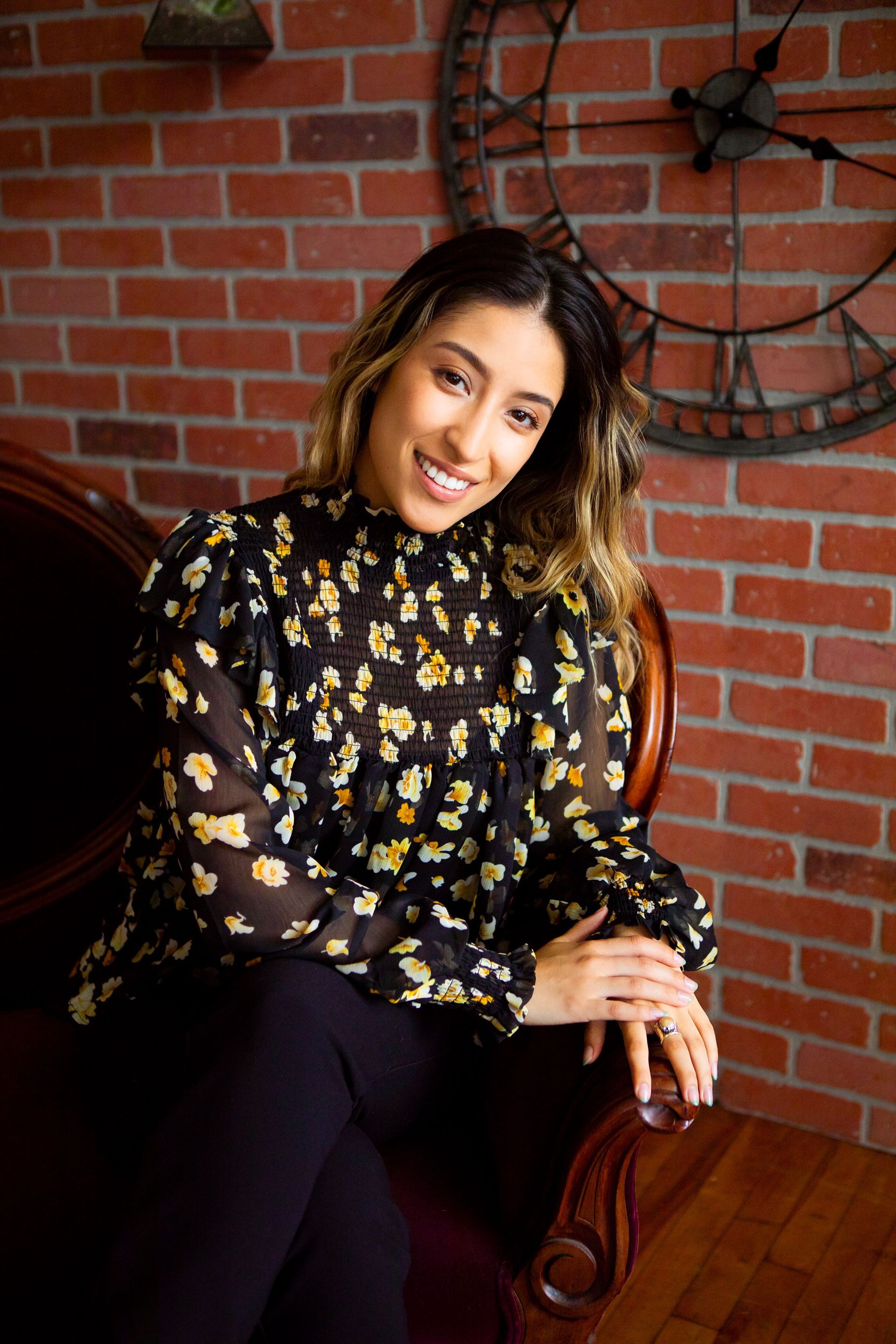 A woman is sitting in a chair in front of a brick wall.
