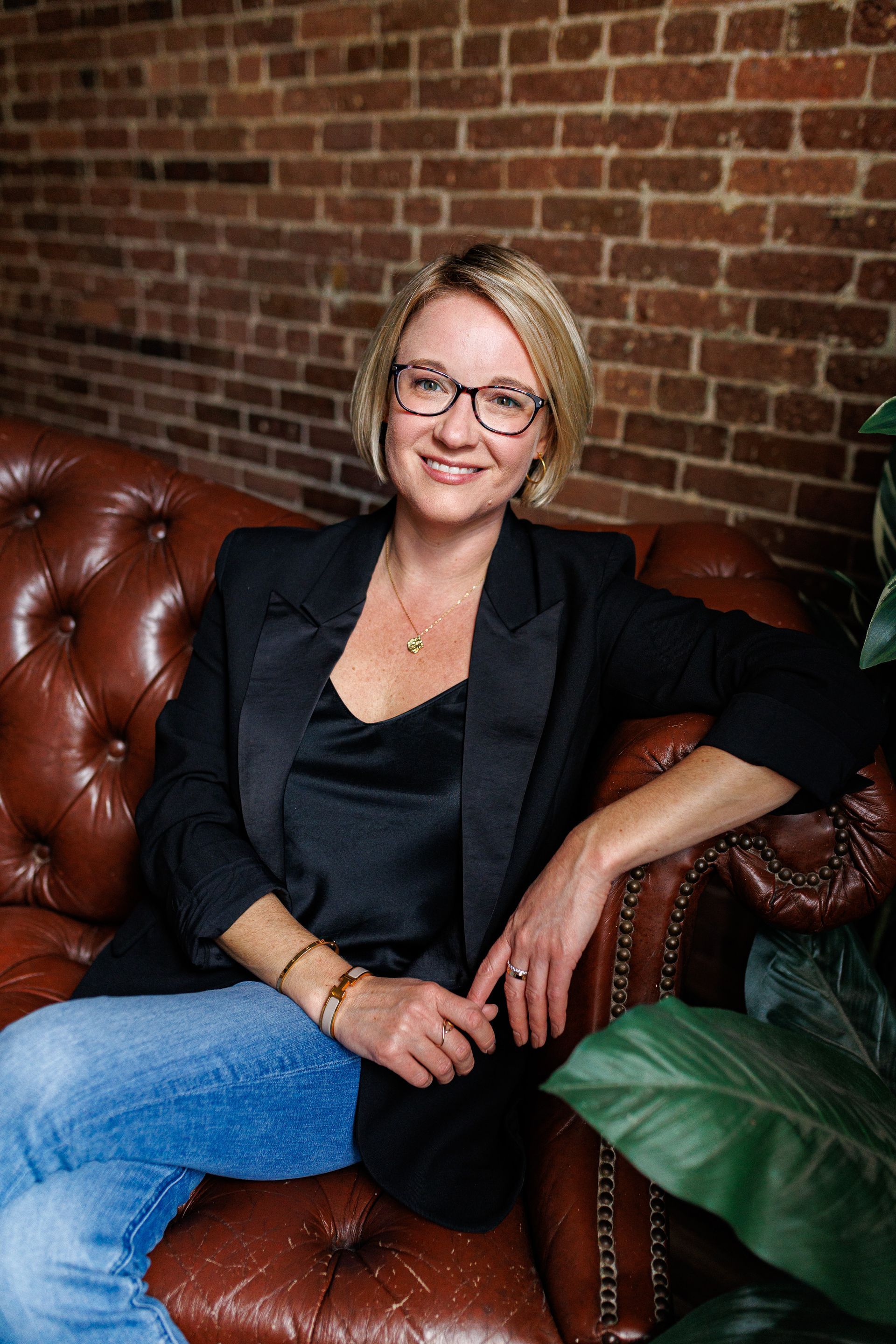 A woman is sitting on a leather couch in front of a brick wall.