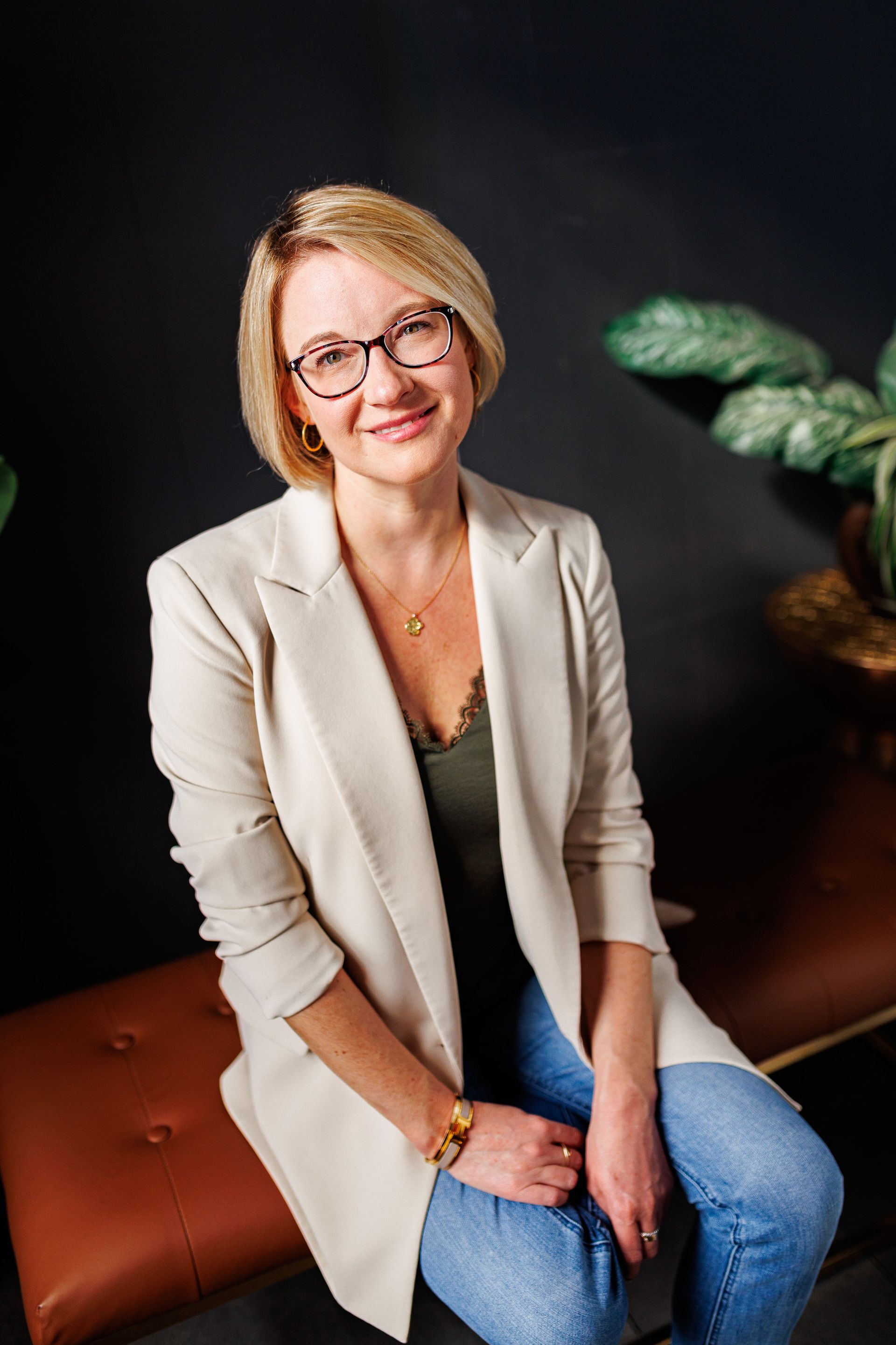 A woman wearing glasses and a white jacket is sitting on a bench.