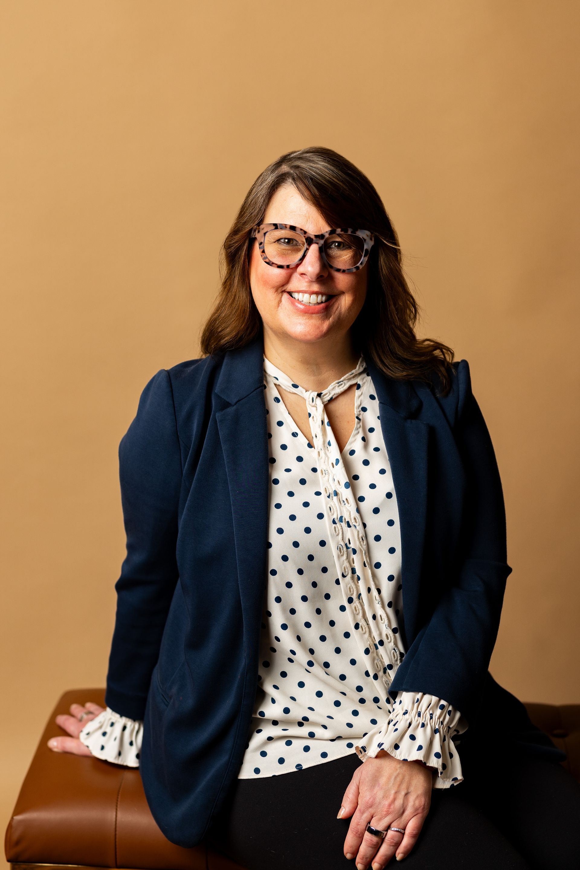 A woman wearing glasses and a polka dot shirt is sitting on a bench.