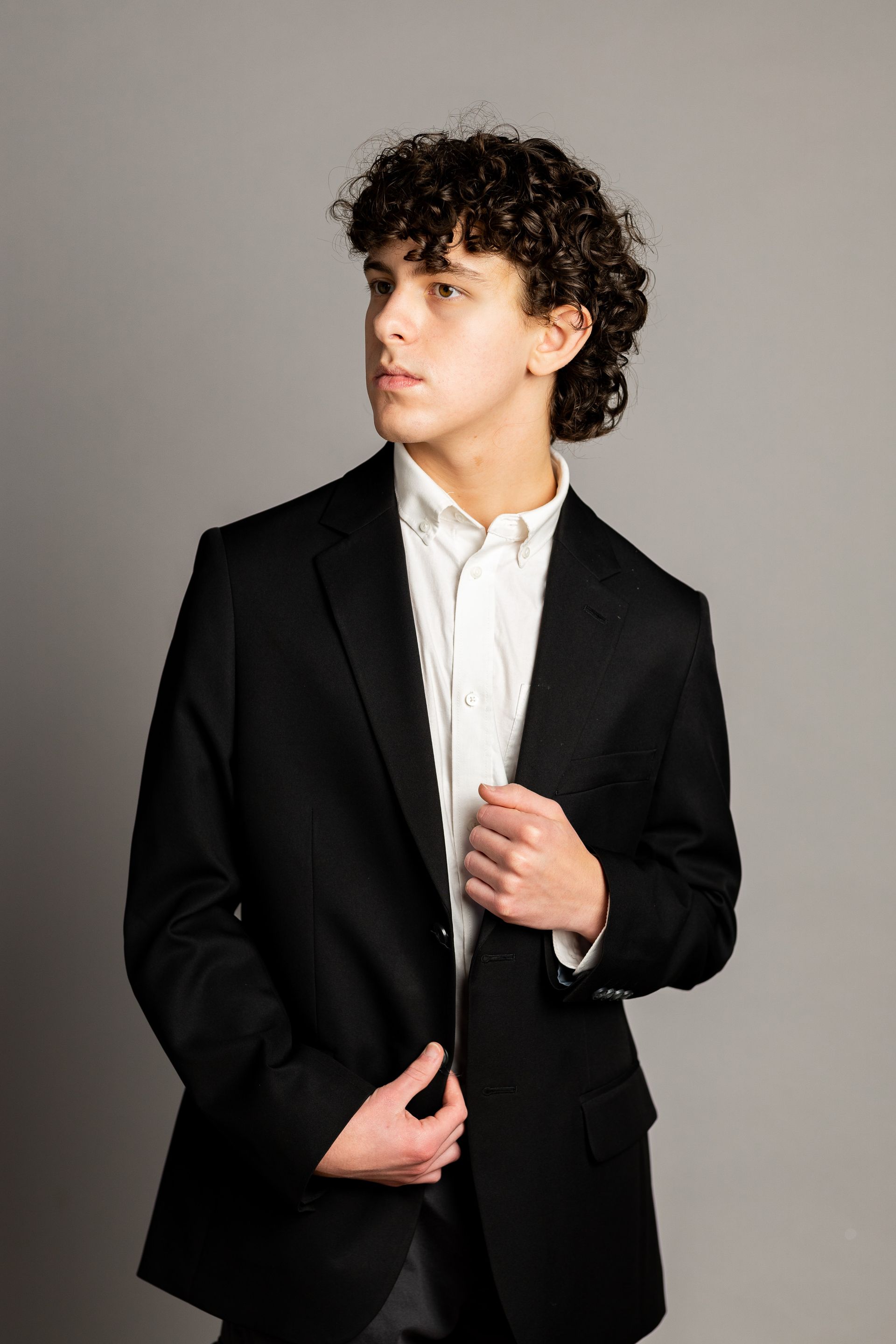 A young man with curly hair is wearing a black jacket and white shirt.