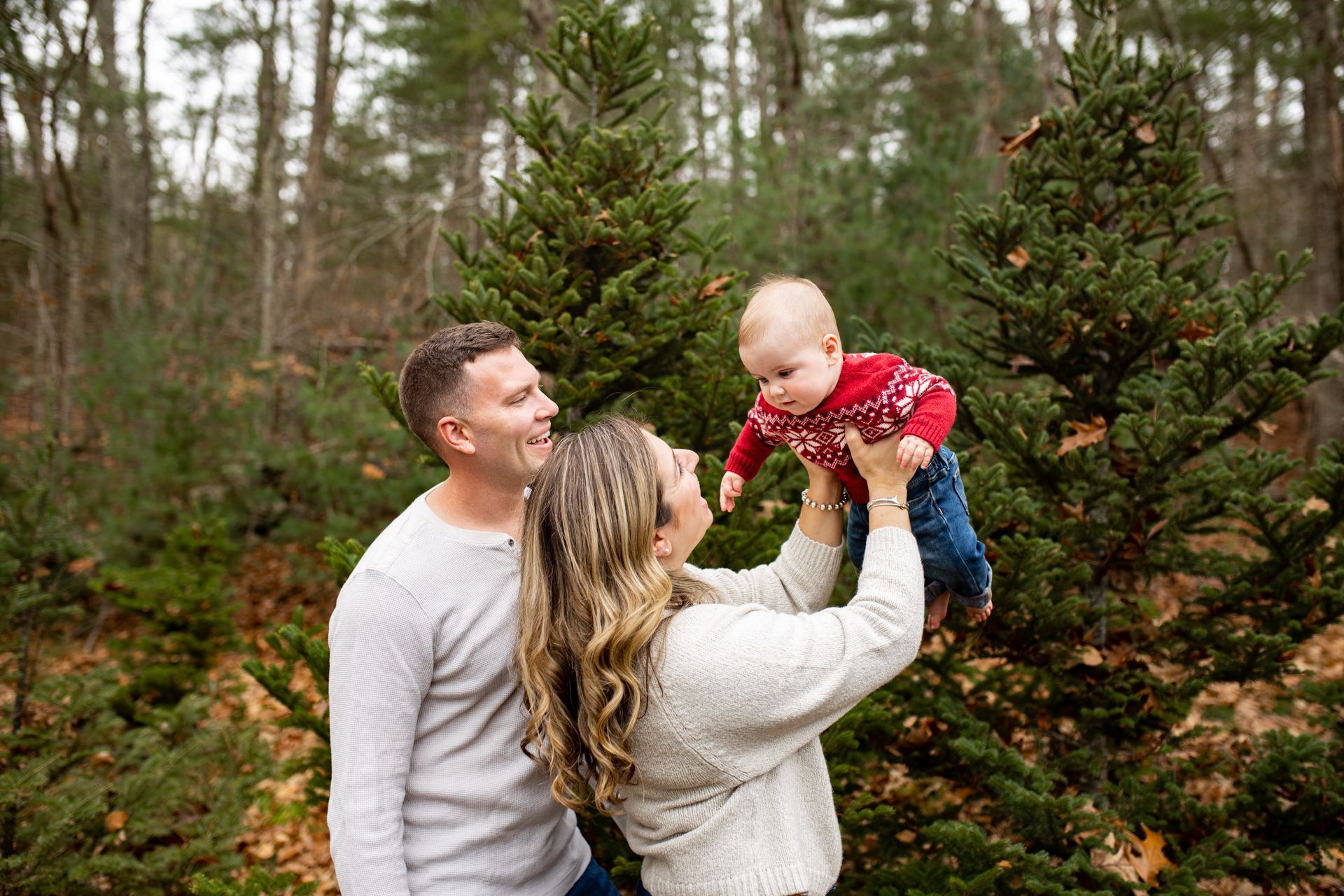 A woman is holding a baby in her arms in front of a christmas tree.