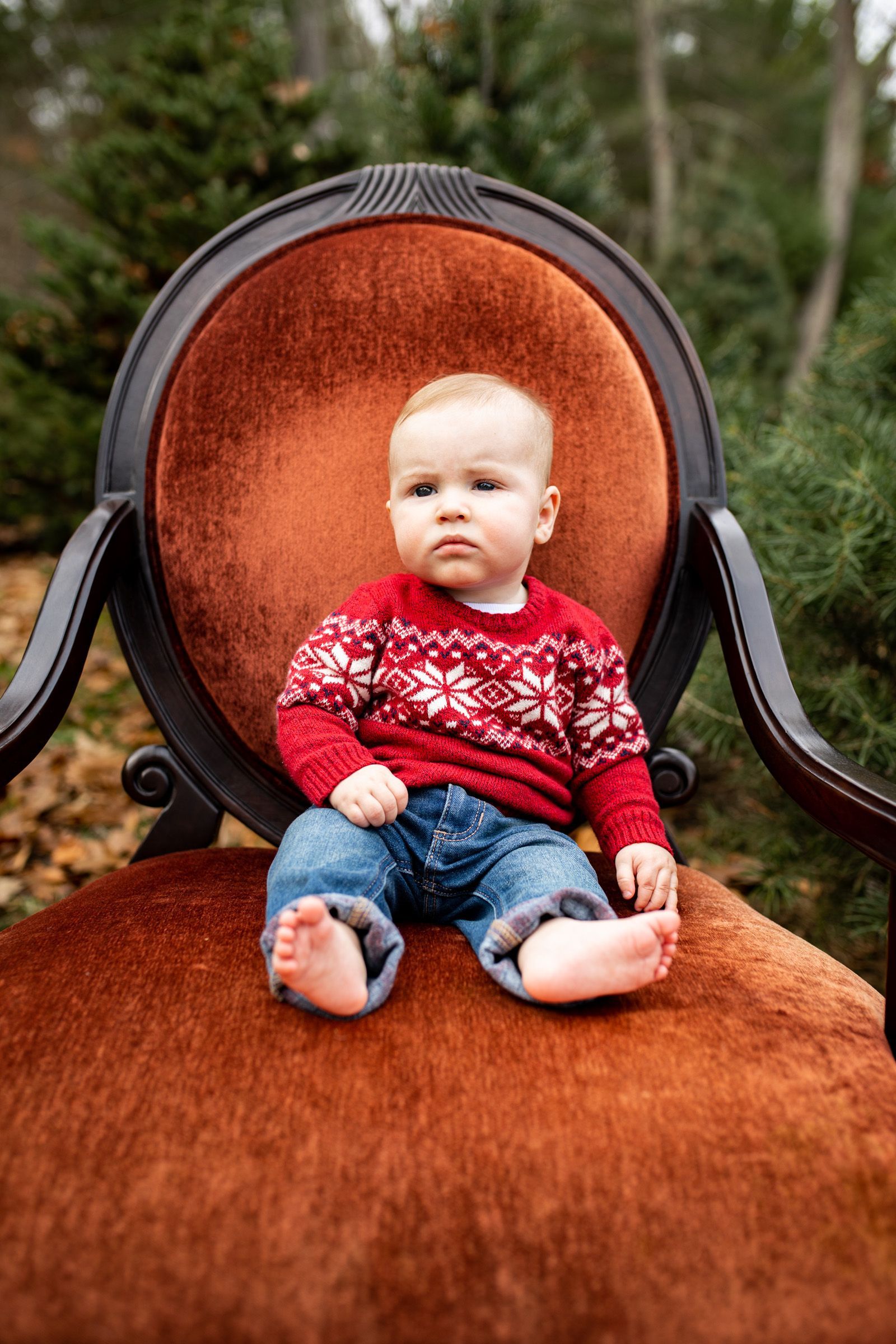 A baby is sitting in a chair wearing a red sweater.