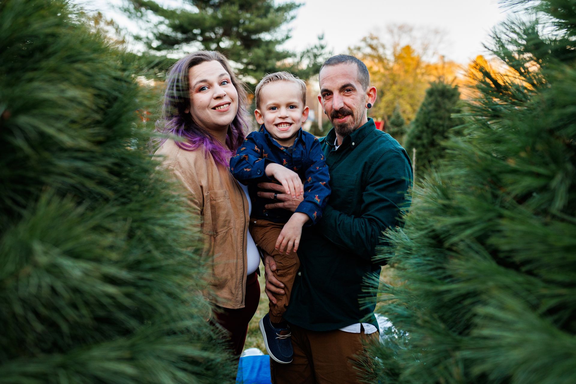 A family is posing for a picture in a christmas tree farm.