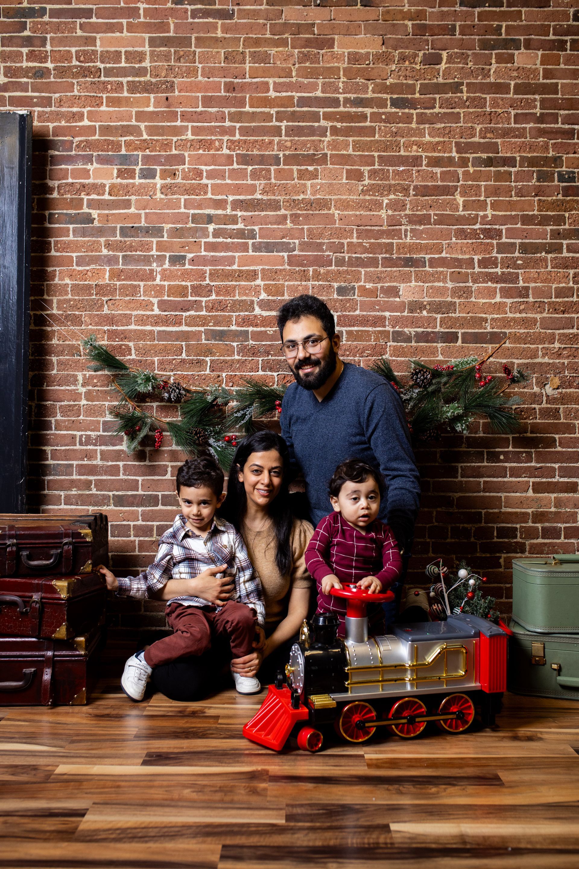 A family is posing for a picture with a toy train in front of a brick wall.