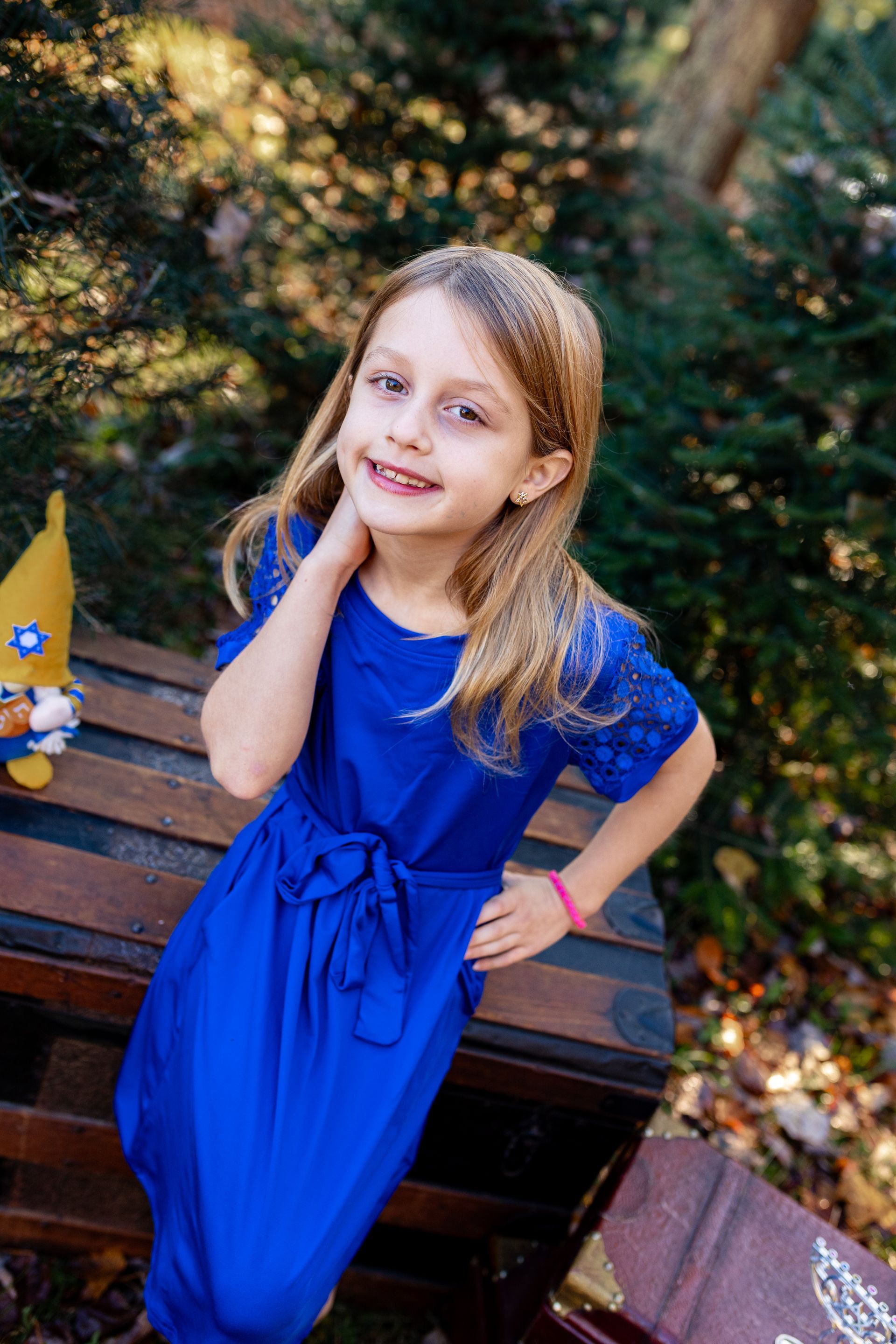 A little girl in a blue dress is sitting on a wooden bench.