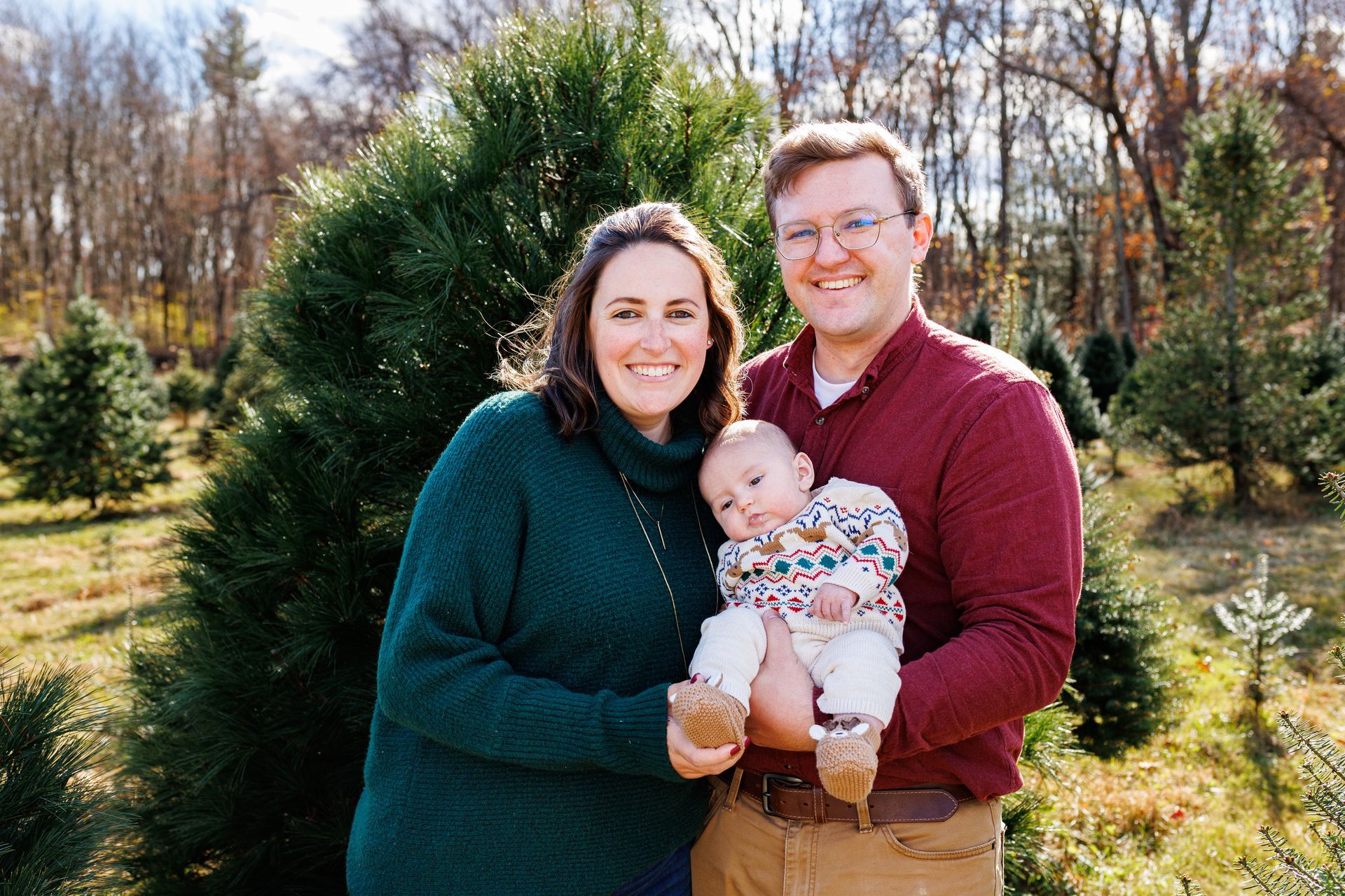 A man and woman are holding a baby in front of a christmas tree.