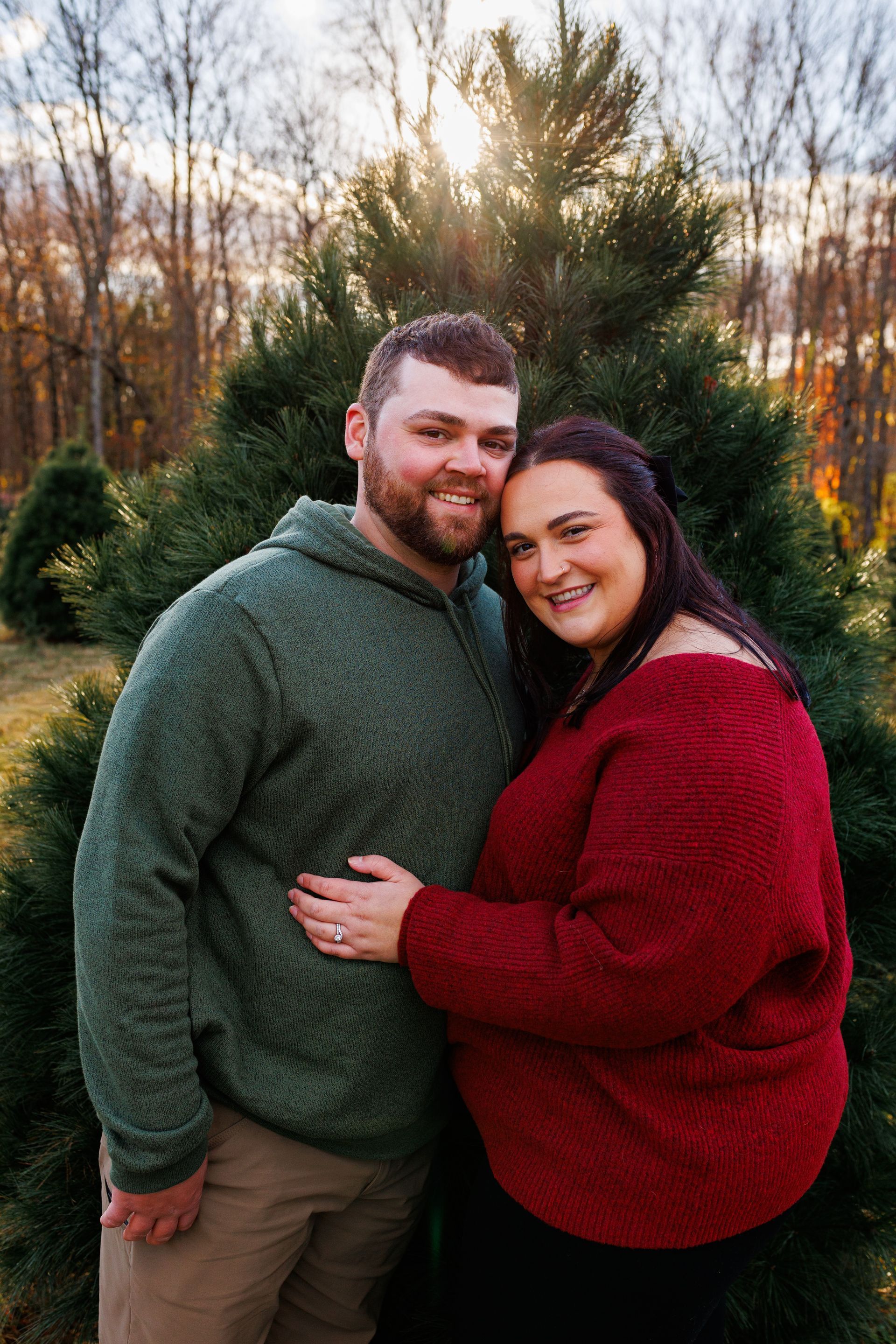 A man and a woman are posing for a picture in front of a christmas tree.