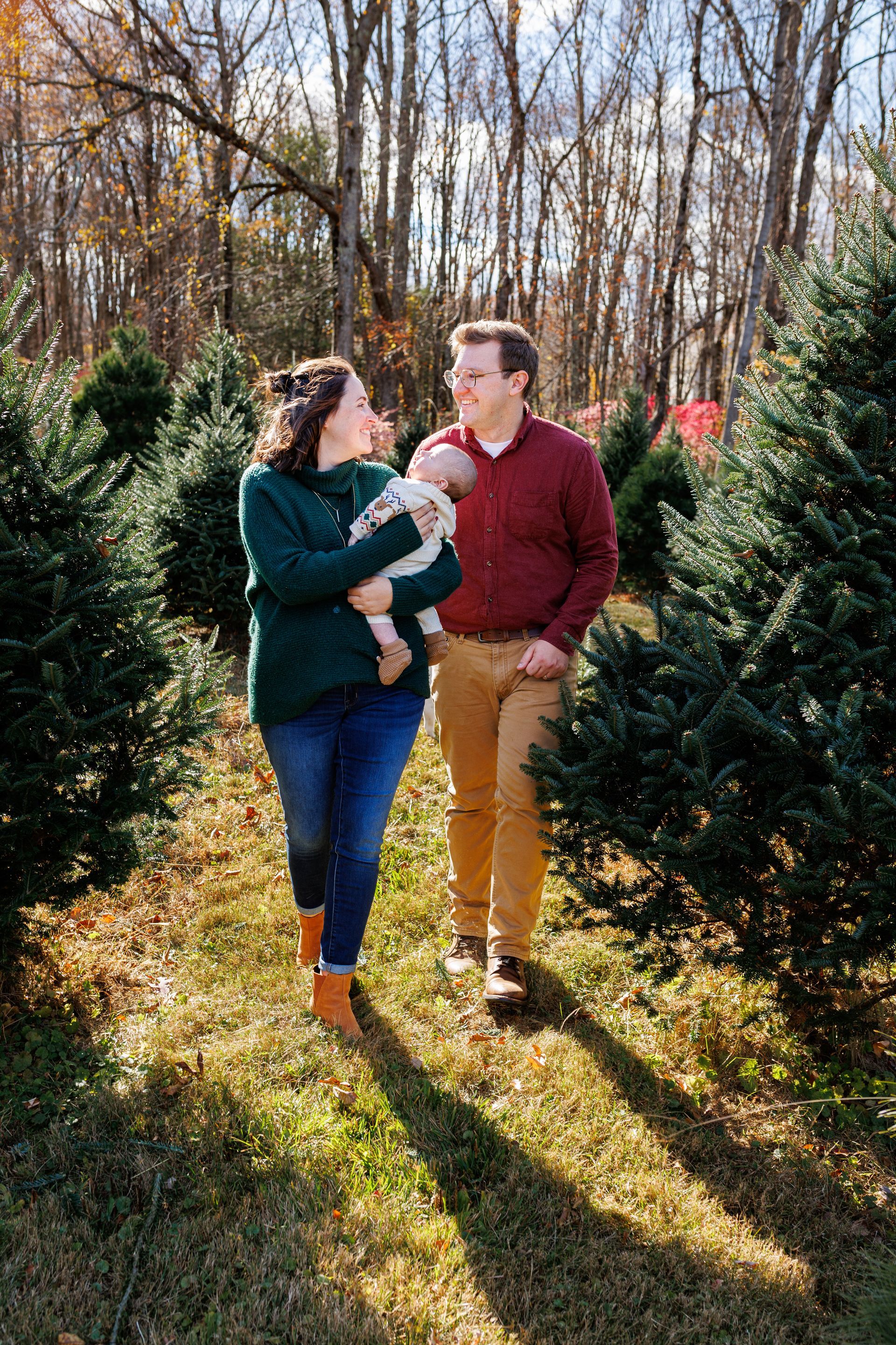 A family is walking through a christmas tree farm holding a baby.