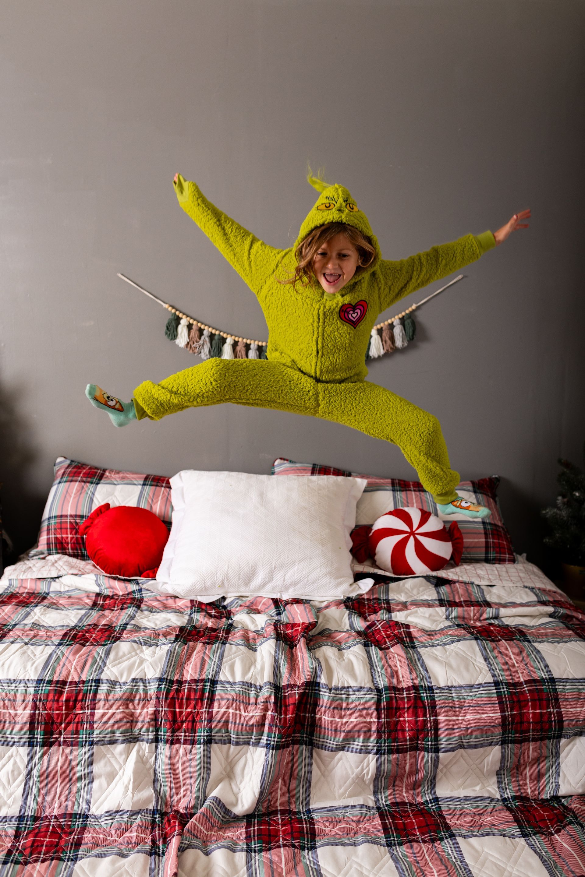 A little girl in a green pajamas is jumping on a bed.