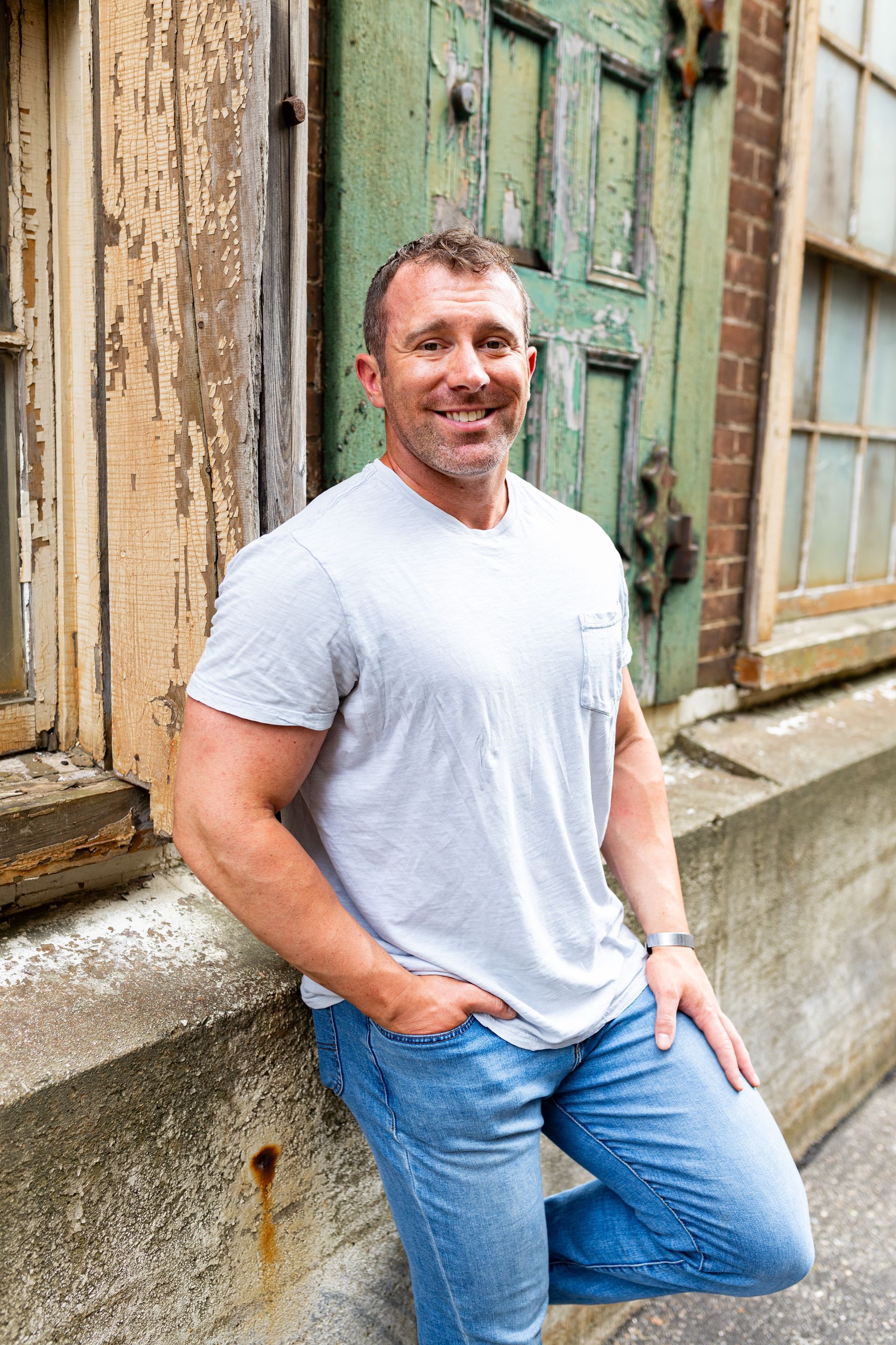 A man is leaning against a wall in front of a green door.