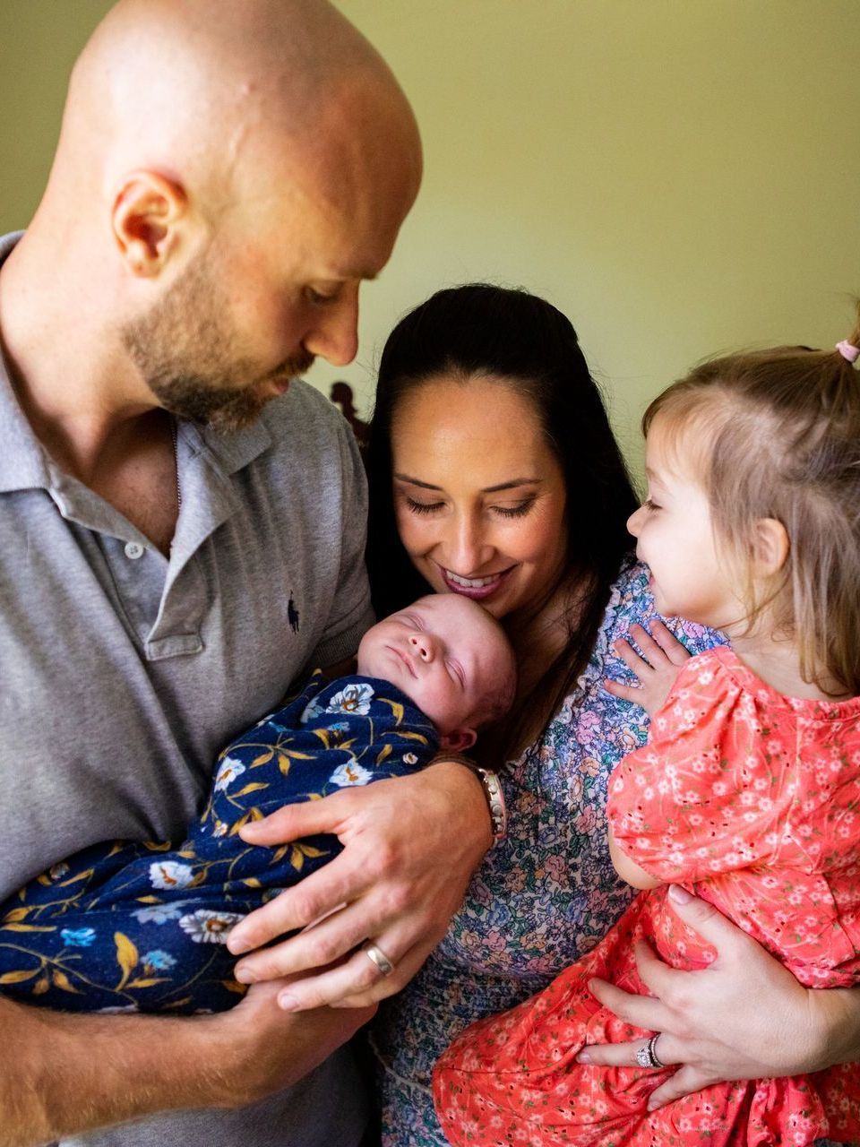 A man and woman are holding a newborn baby while a little girl looks on.