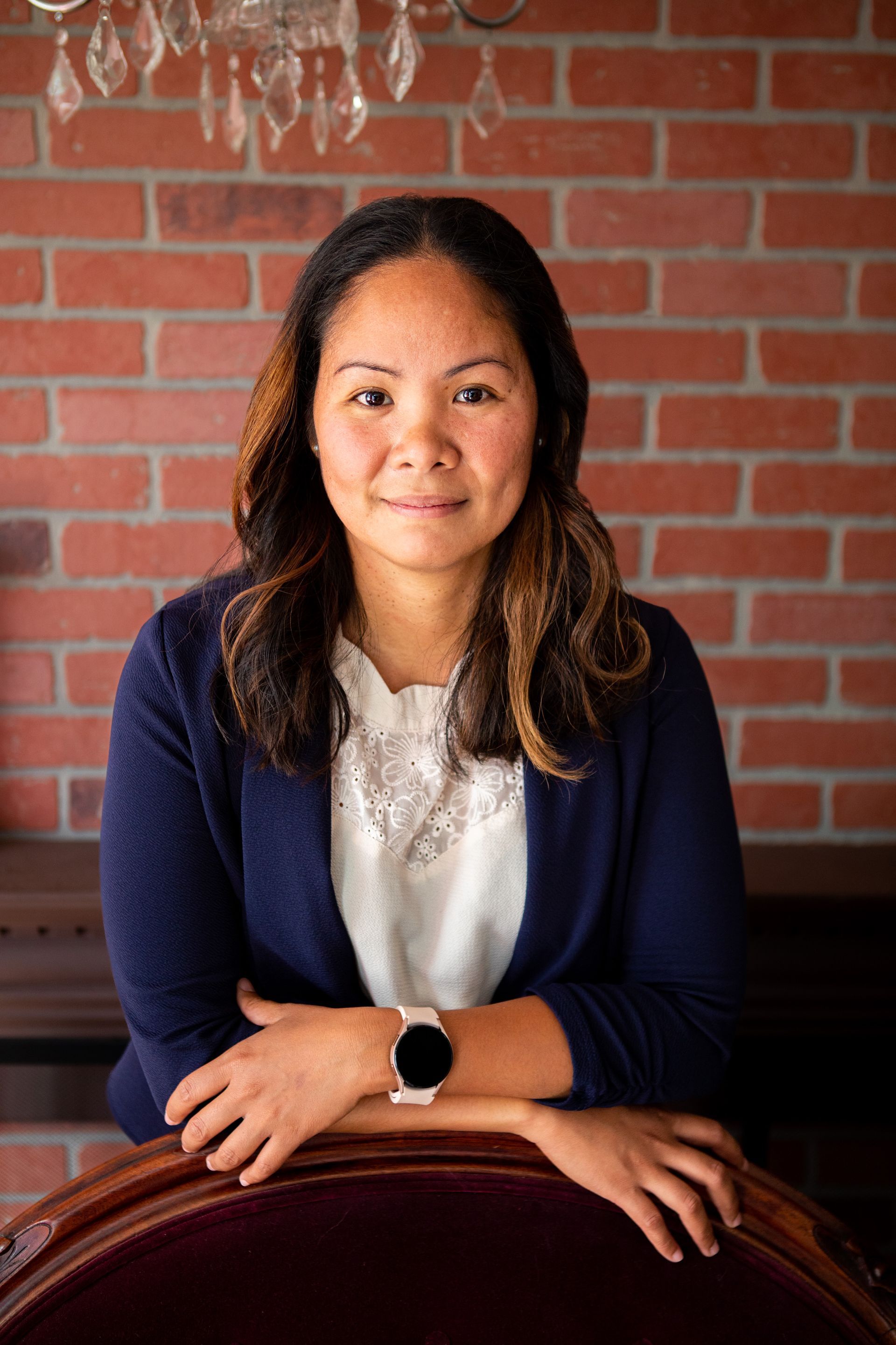 A woman is sitting on a chair in front of a brick wall.