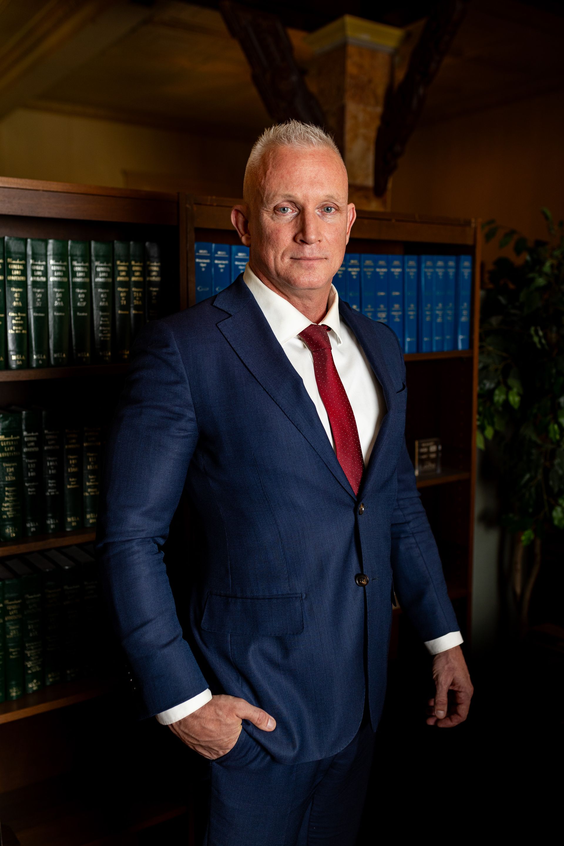 A man in a suit and tie is standing in front of a bookshelf.