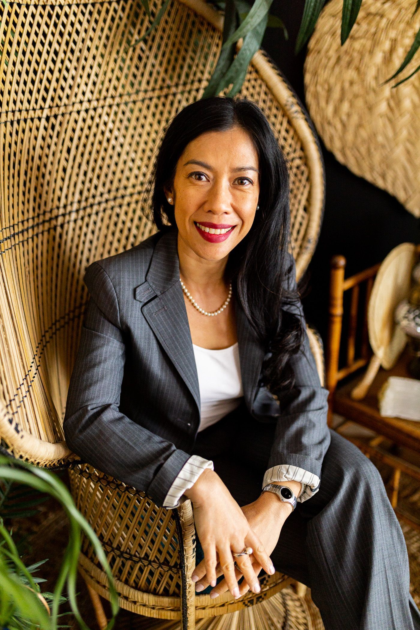 A woman in a suit is sitting in a wicker chair.