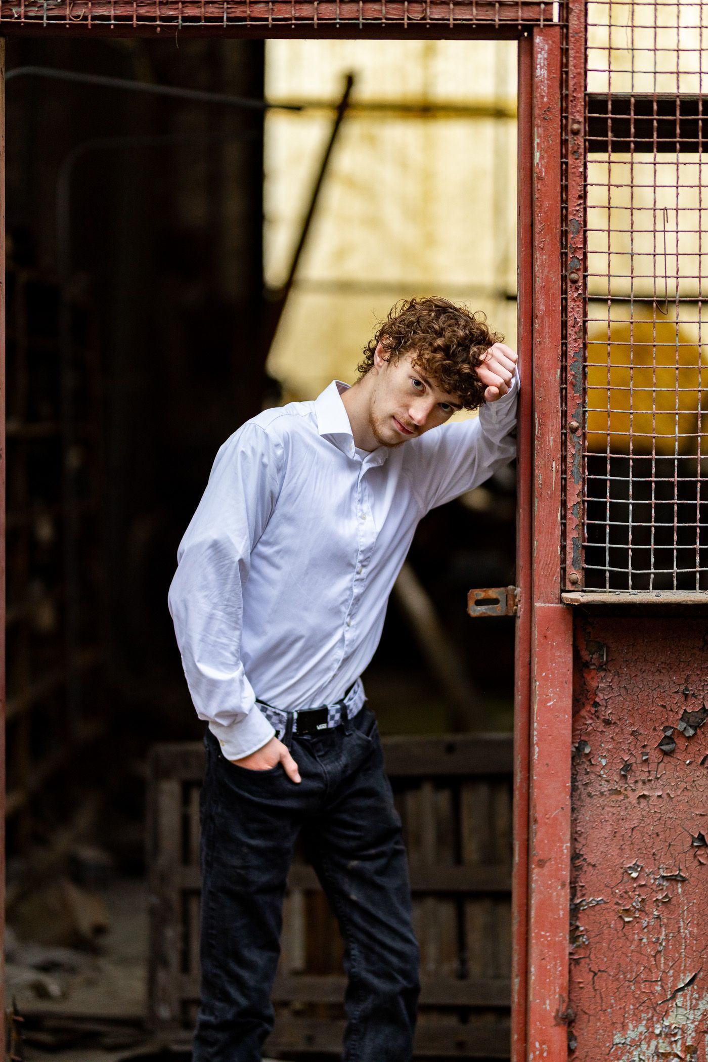 Photography MA -A man in a white shirt and black jeans is leaning against a red door.